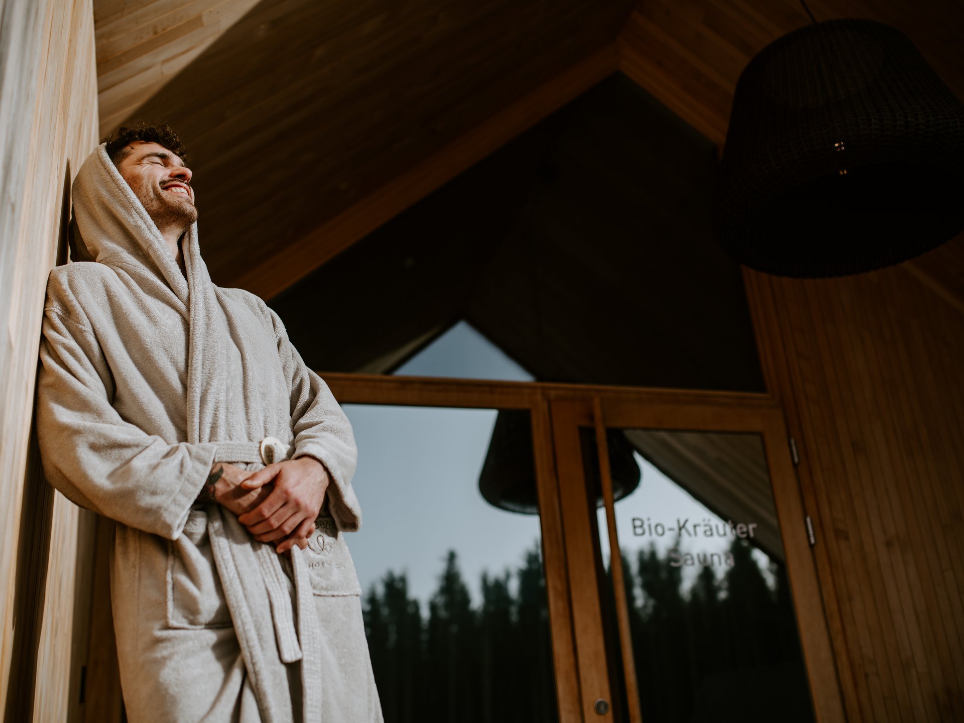 Seezeit re.connect – Bewusste Verbindung mit Natur & Kraftort Mann in Bademantel entspannt vor Sauna-Tür im Holzhaus