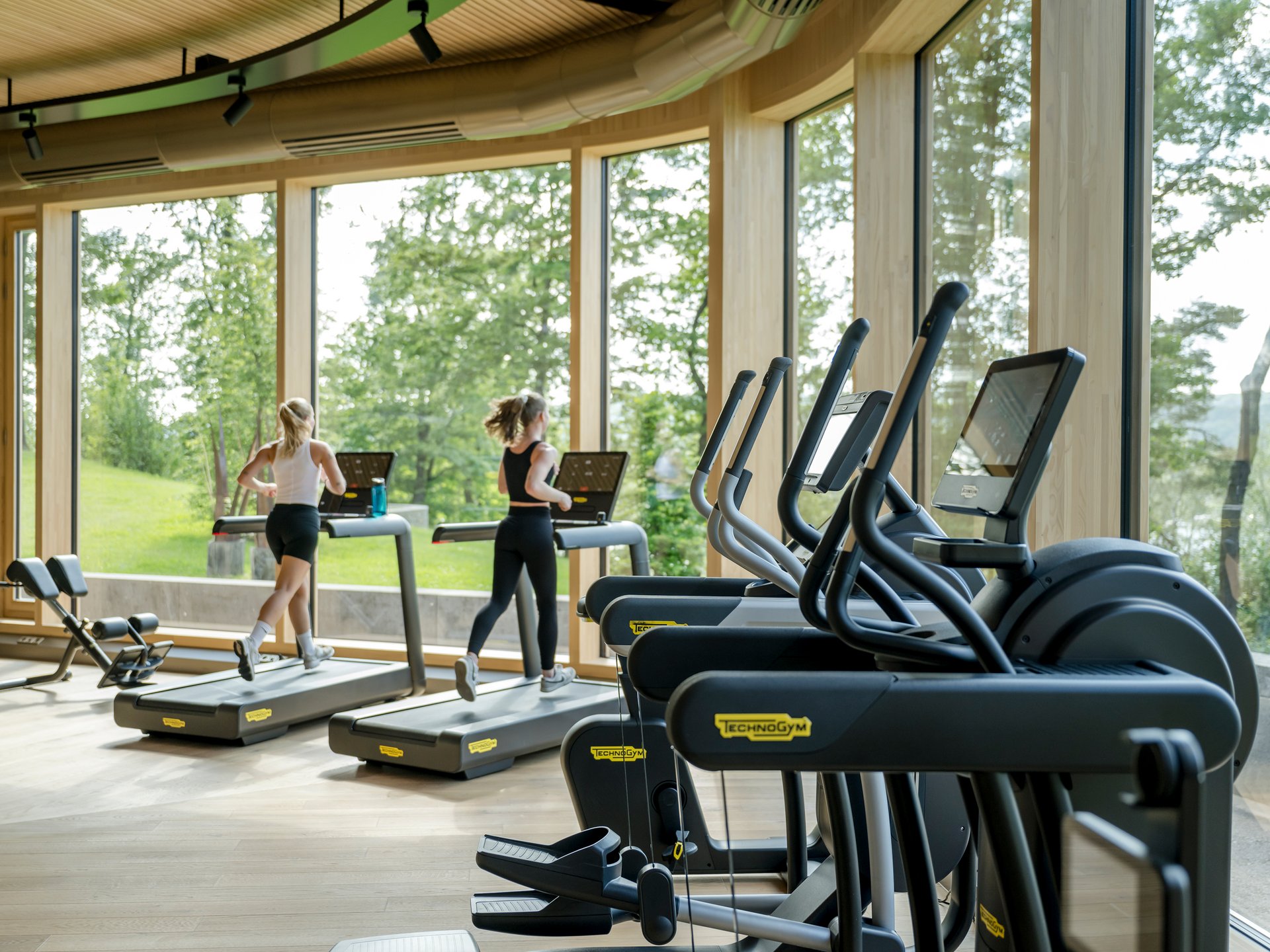 Seezeit re.connect – Bewusste Verbindung mit Natur & Kraftort Zwei Frauen laufen auf Laufbändern in einem Fitnessstudio mit großen Fenstern
