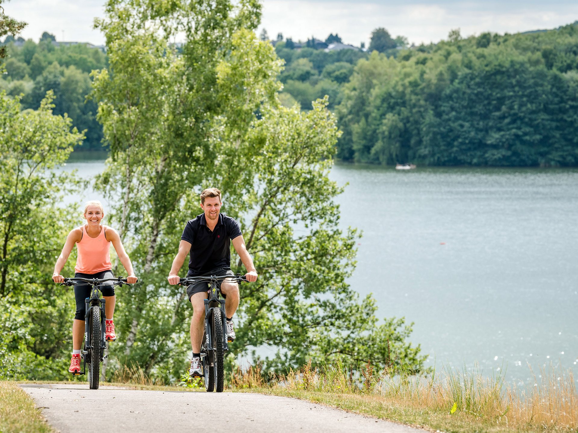 Urlaub am Bostalsee: die Highlights der Region Zwei Personen fahren mit Fahrrädern auf einem Weg neben einem See und Bäumen