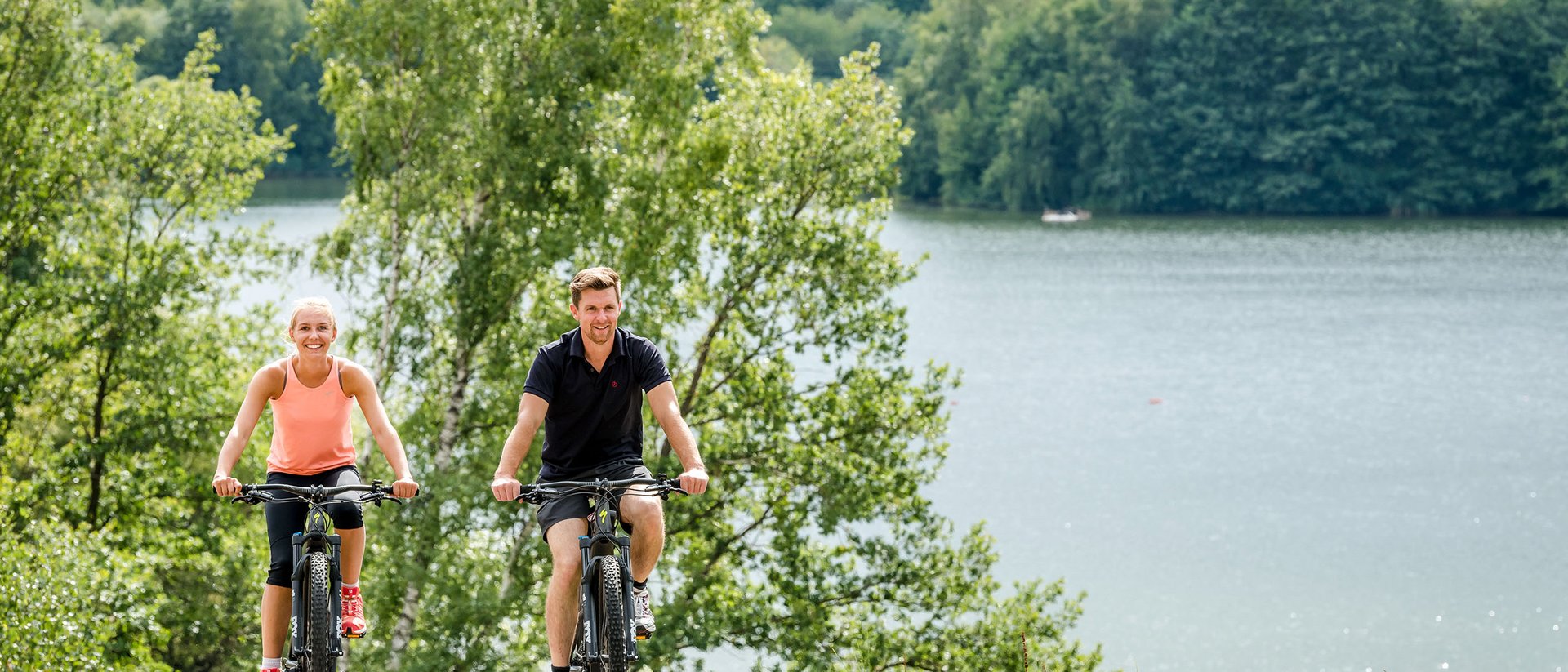 Seezeitlodge: Bildergalerie Zwei Personen fahren mit Fahrrädern auf einem Weg neben einem See und Bäumen