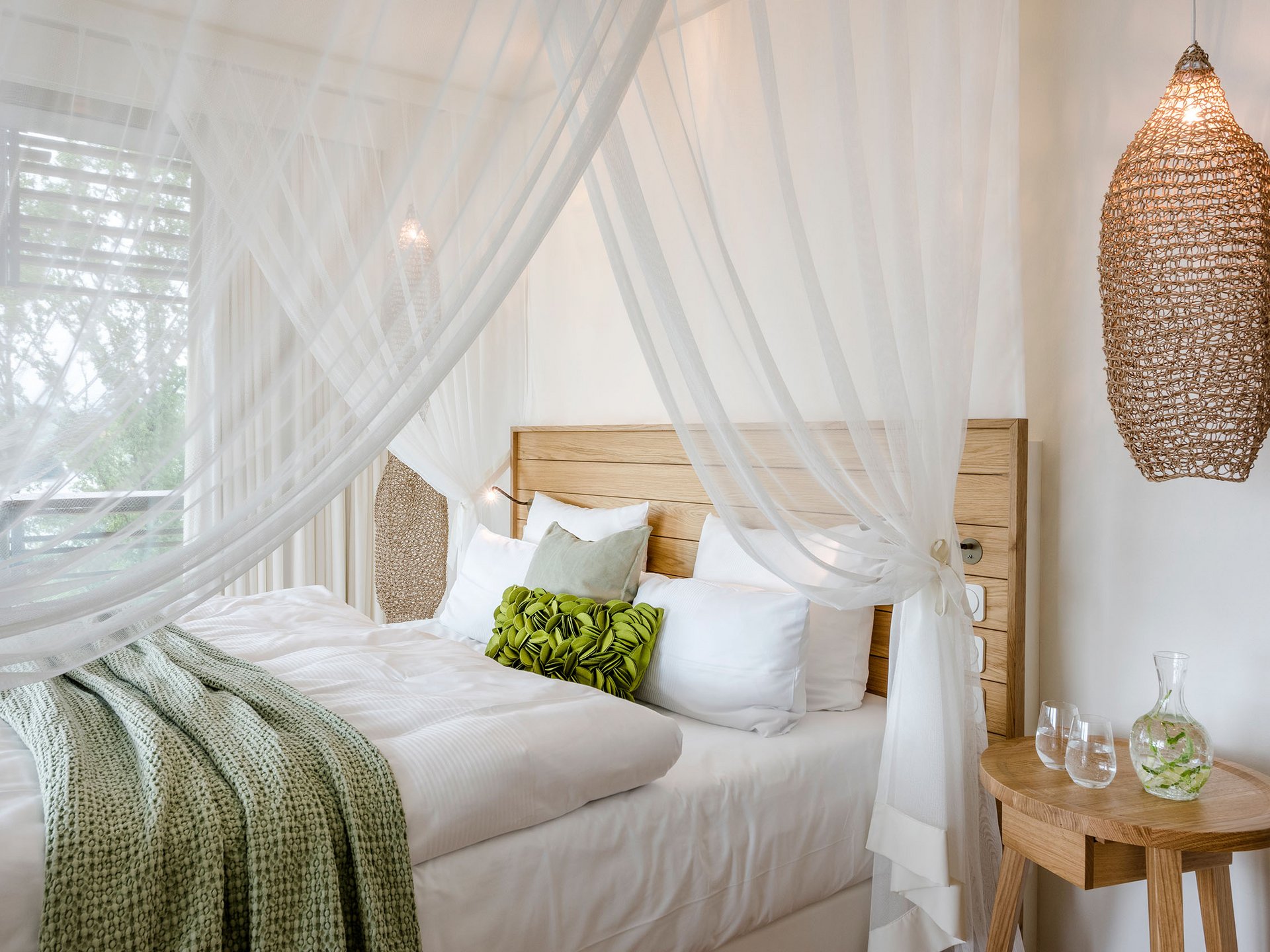 Le Seezeitlodge : votre hôtel au lac de Bostal Lit confortable avec cadre en bois, rideaux blancs et coussin vert dans une chambre d'hôtel