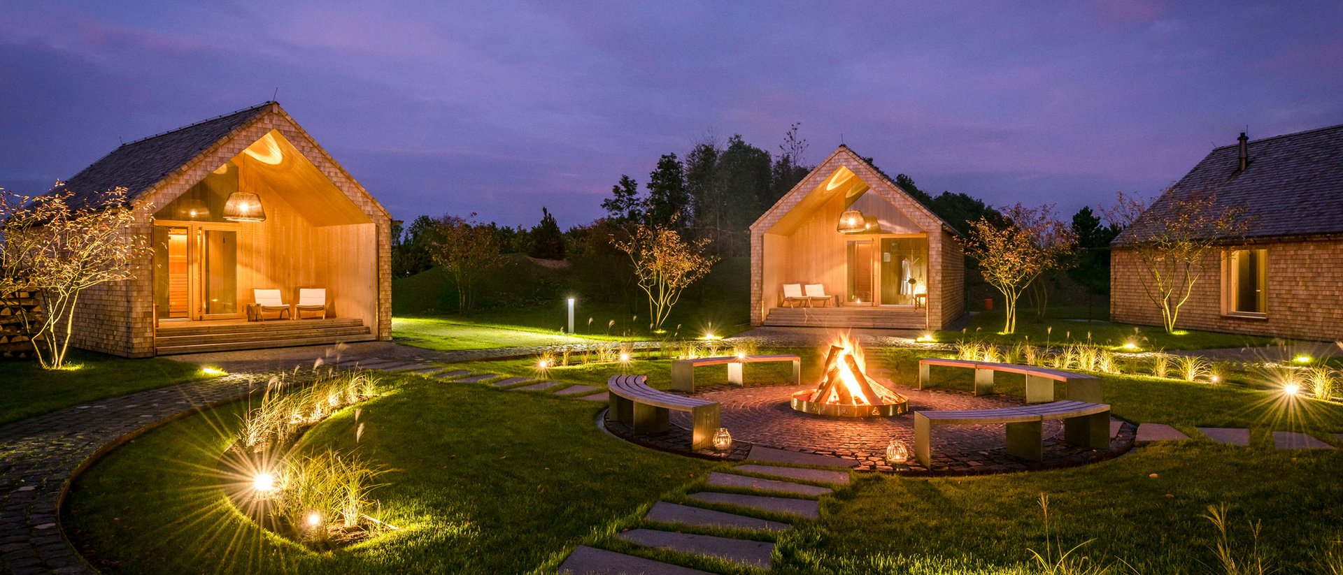 Seezeitlodge: Ihr Wellnesshotel am Bostalsee für pure Erholung Beleuchtete Holzhütten und Feuerstelle bei Nacht in gepflegtem Garten