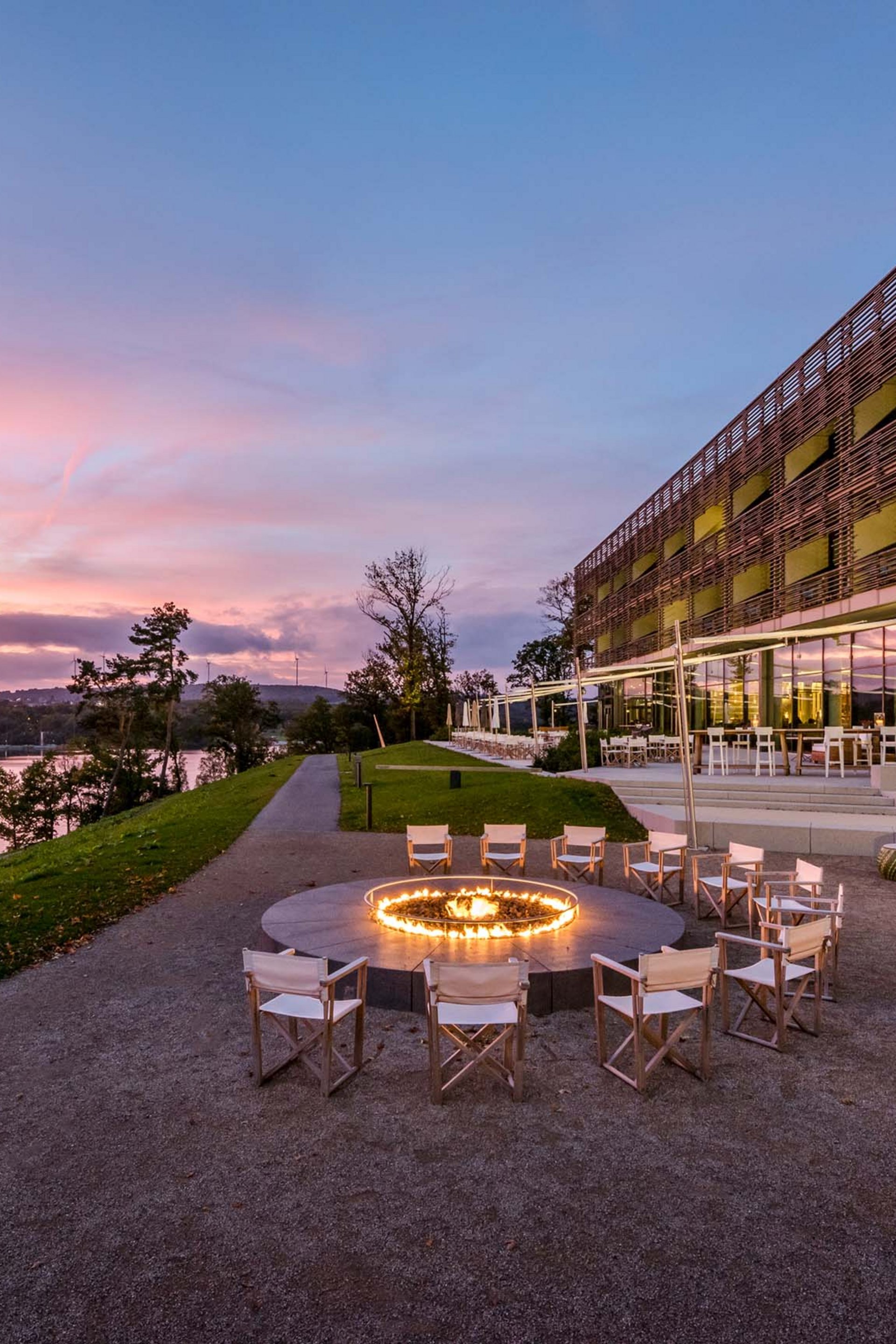 Seezeitlodge : Galerie photos Espace assis avec feu circulaire près d'un bâtiment moderne au bord de la rivière au coucher du soleil