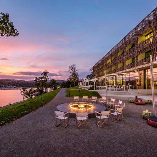 Design hotel Germany: your retreat at Lake Bostalsee Seating area with fire pit beside modern building and river at sunset