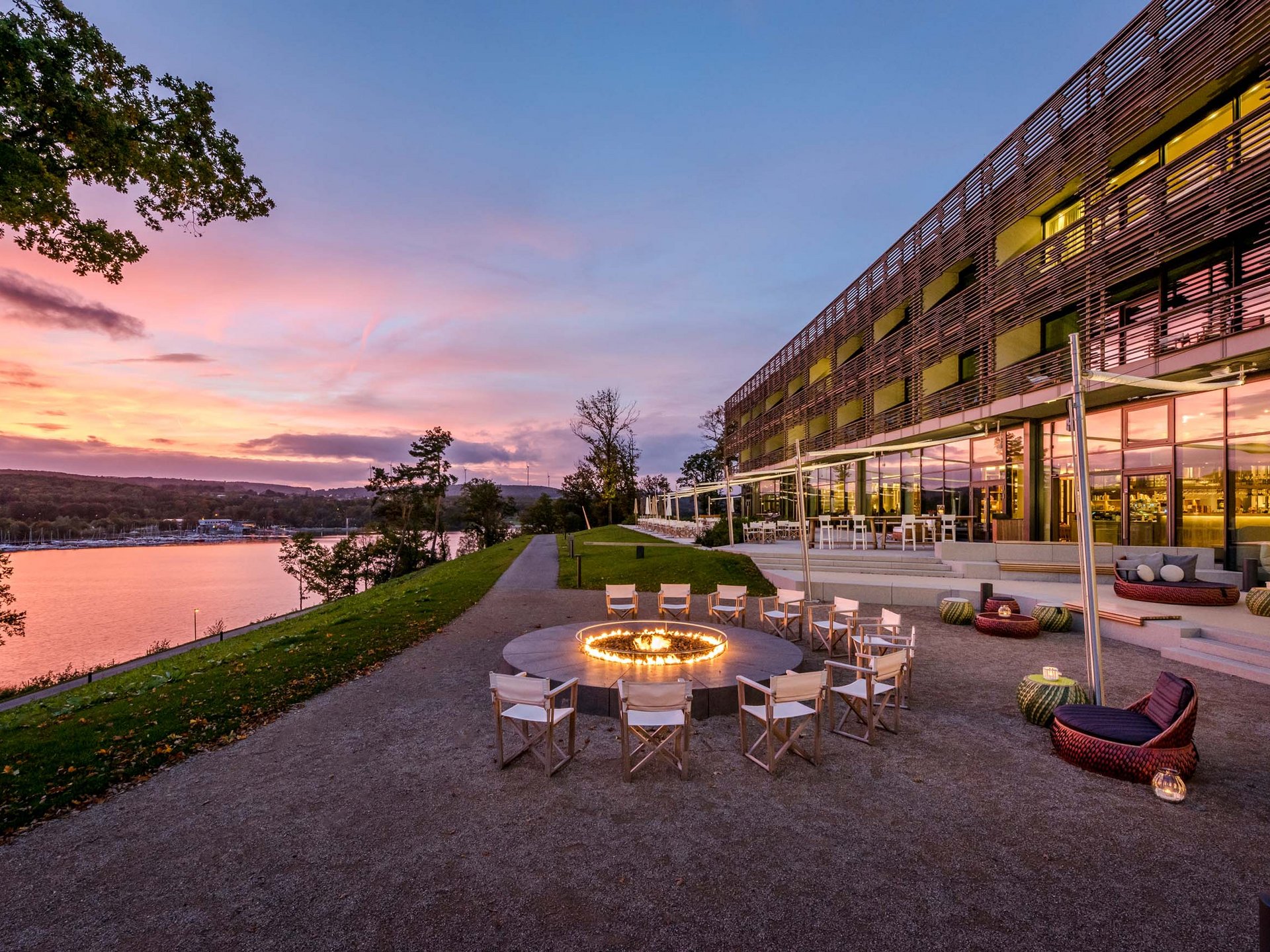 Le Seezeitlodge : votre hôtel au lac de Bostal Espace assis avec feu circulaire près d'un bâtiment moderne au bord de la rivière au coucher du soleil