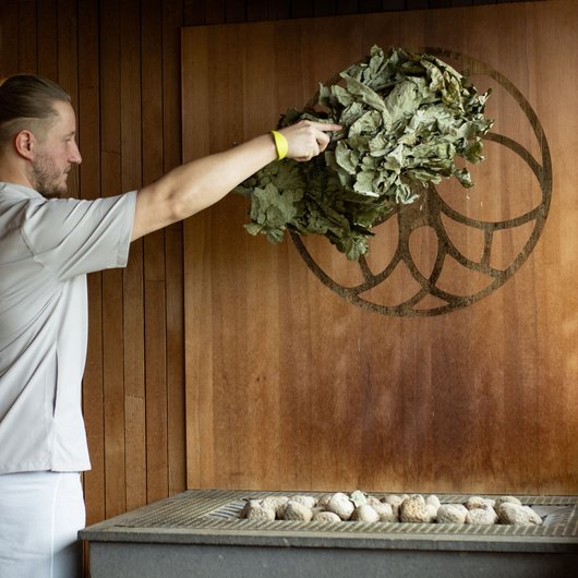 Seezeitlodge: Ihr Wellnesshotel am Bostalsee für pure Erholung Mann wedelt mit Birkenzweigen in Sauna vor Heizgerät