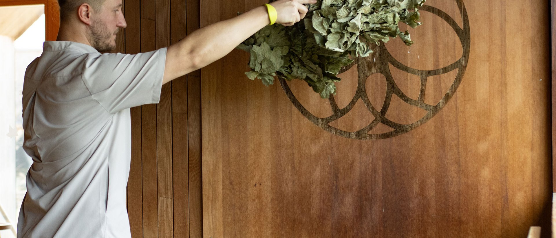 Seezeitlodge : Galerie photos Homme agitant des branches de bouleau dans un sauna devant un poêle
