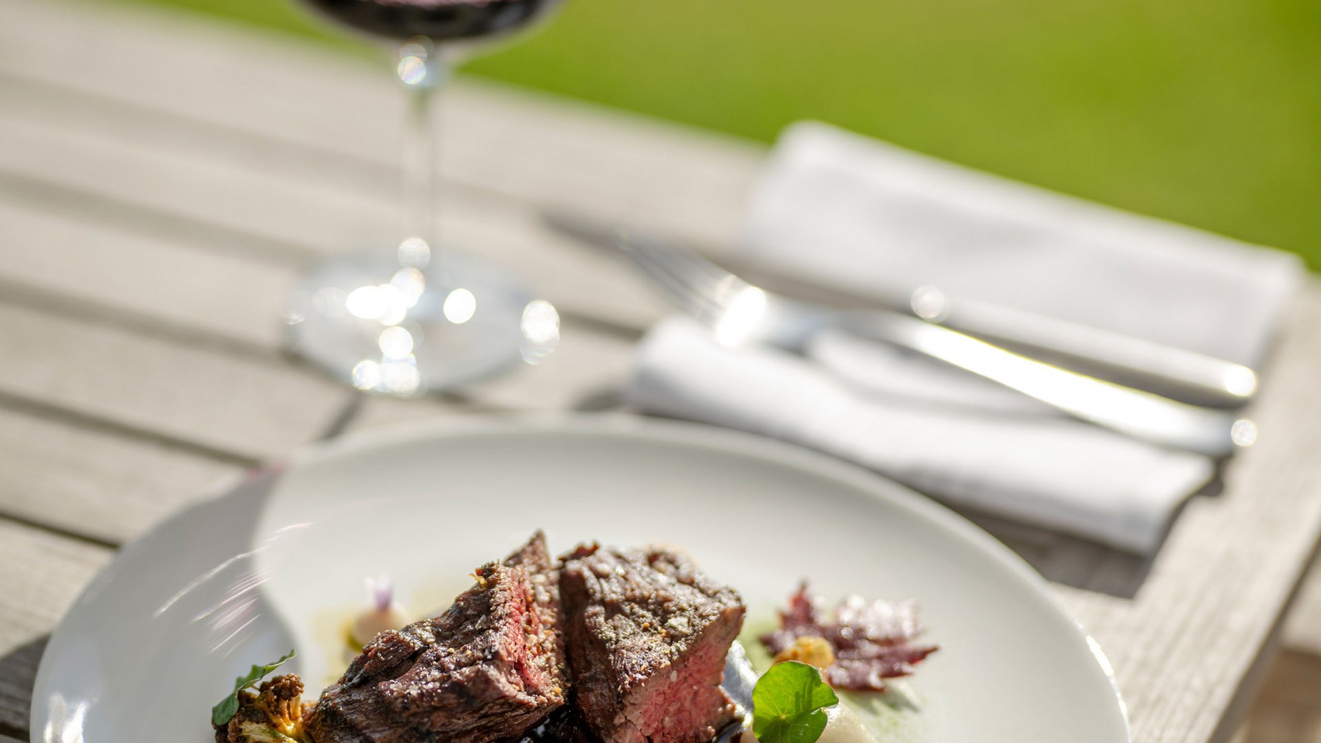 Seezeitlodge: Bildergalerie Steak mit Gemüse auf weißem Teller und Glas Rotwein im Freien
