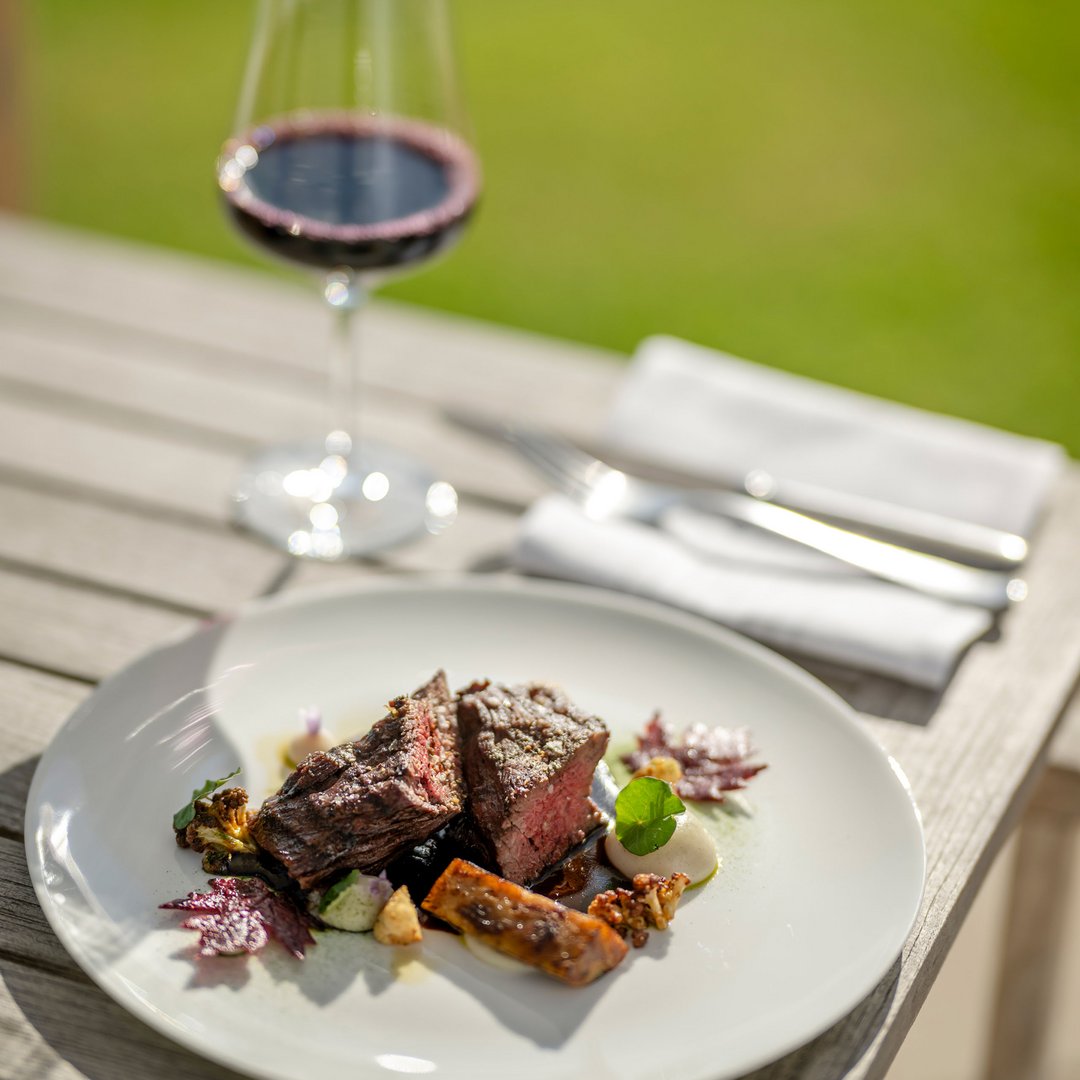 Seezeitlodge : protection des données Steak avec légumes sur assiette blanche et verre de vin rouge en plein air