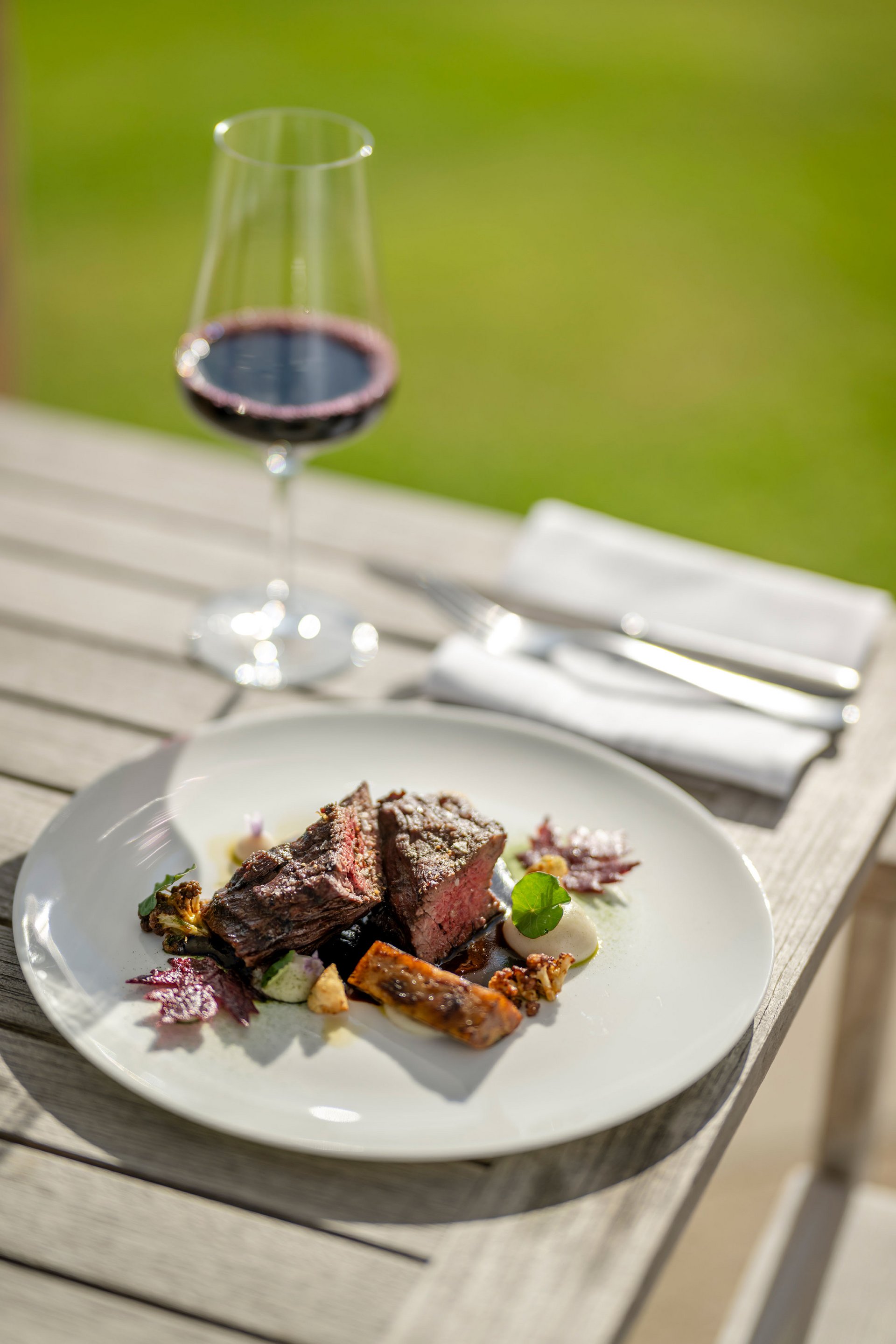 Seezeitlodge : Galerie photos Steak avec légumes sur assiette blanche et verre de vin rouge en plein air