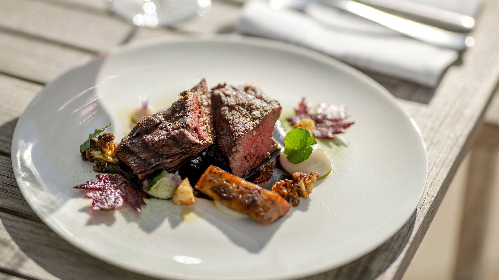 Ihr Genusshotel am Bostalsee Steak mit Gemüse auf weißem Teller und Glas Rotwein im Freien