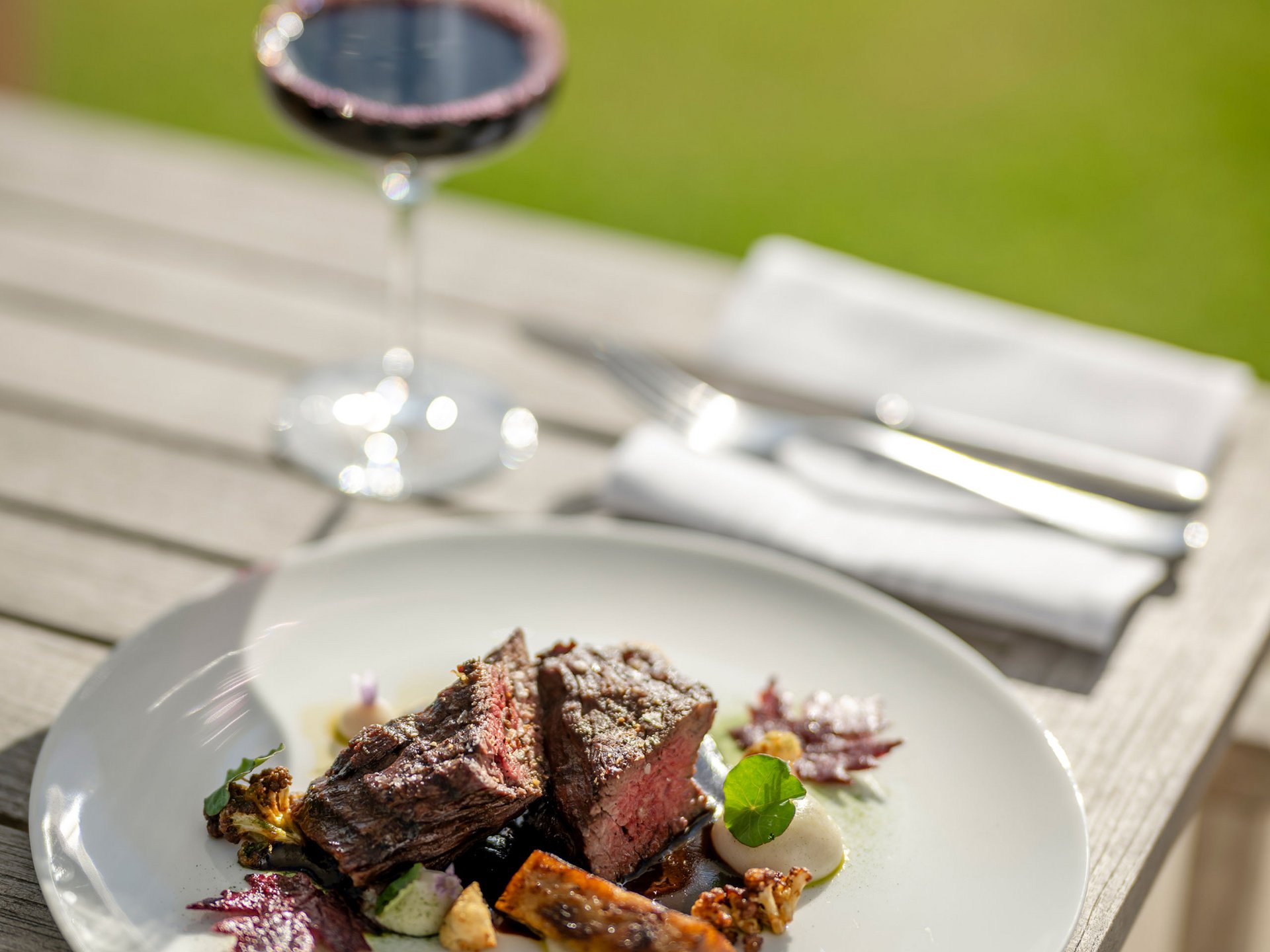Seezeitlodge : Galerie photos Steak avec légumes sur assiette blanche et verre de vin rouge en plein air