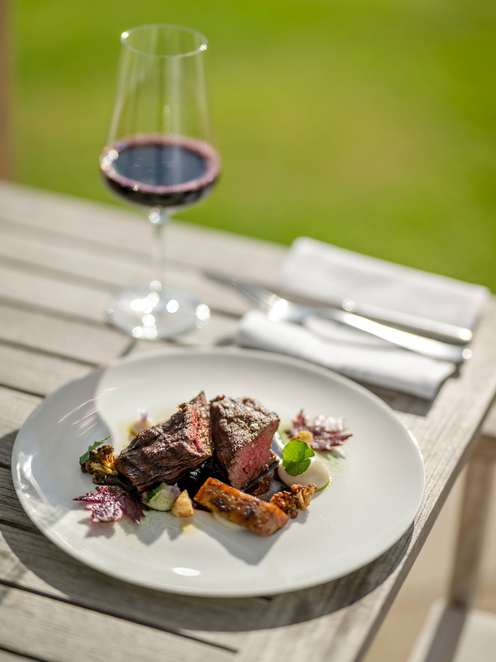 Seezeitlodge : Galerie photos Steak avec légumes sur assiette blanche et verre de vin rouge en plein air