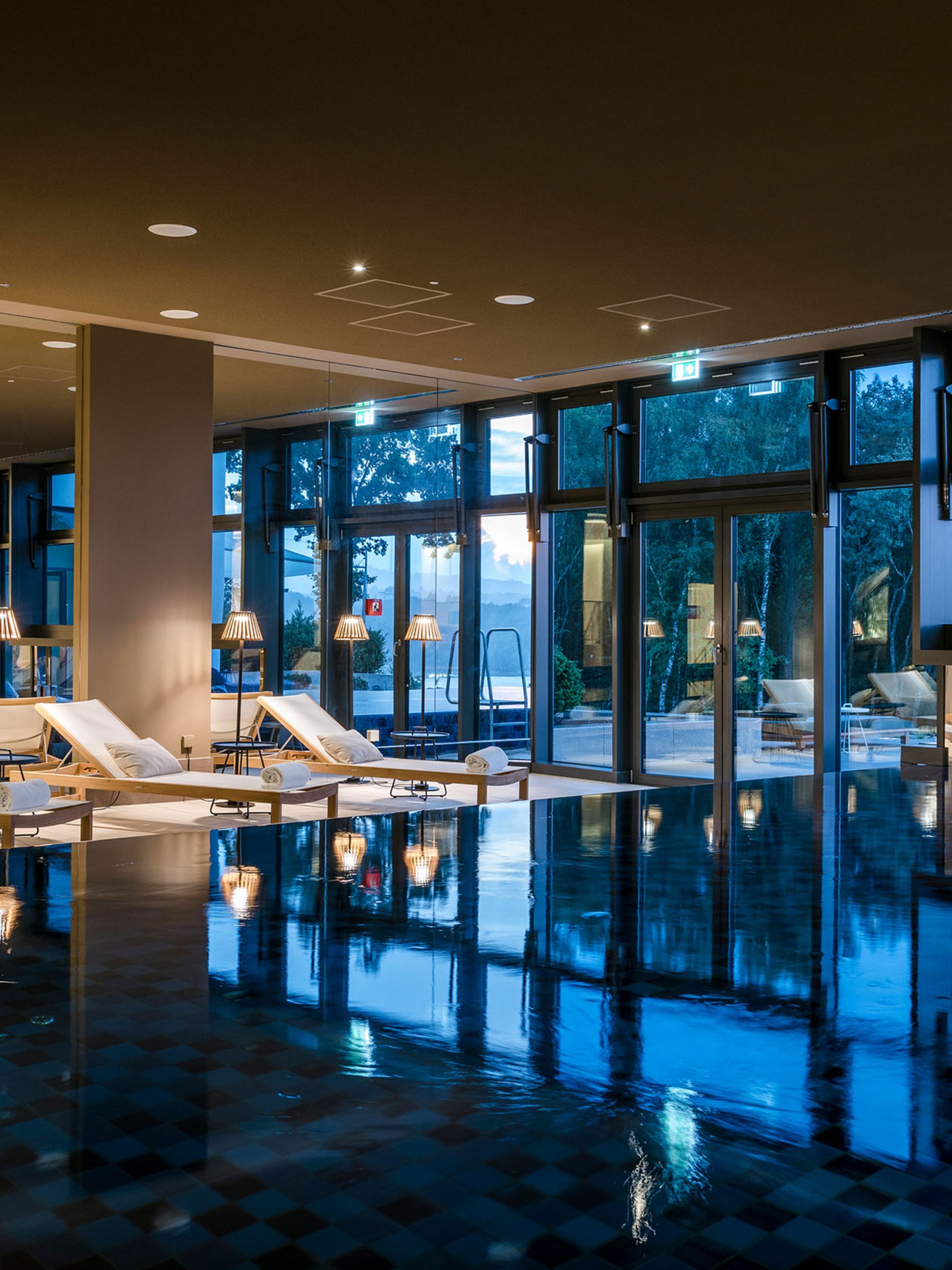 Seezeitlodge : Galerie photos Piscine intérieure avec chaises longues et grandes fenêtres au crépuscule
