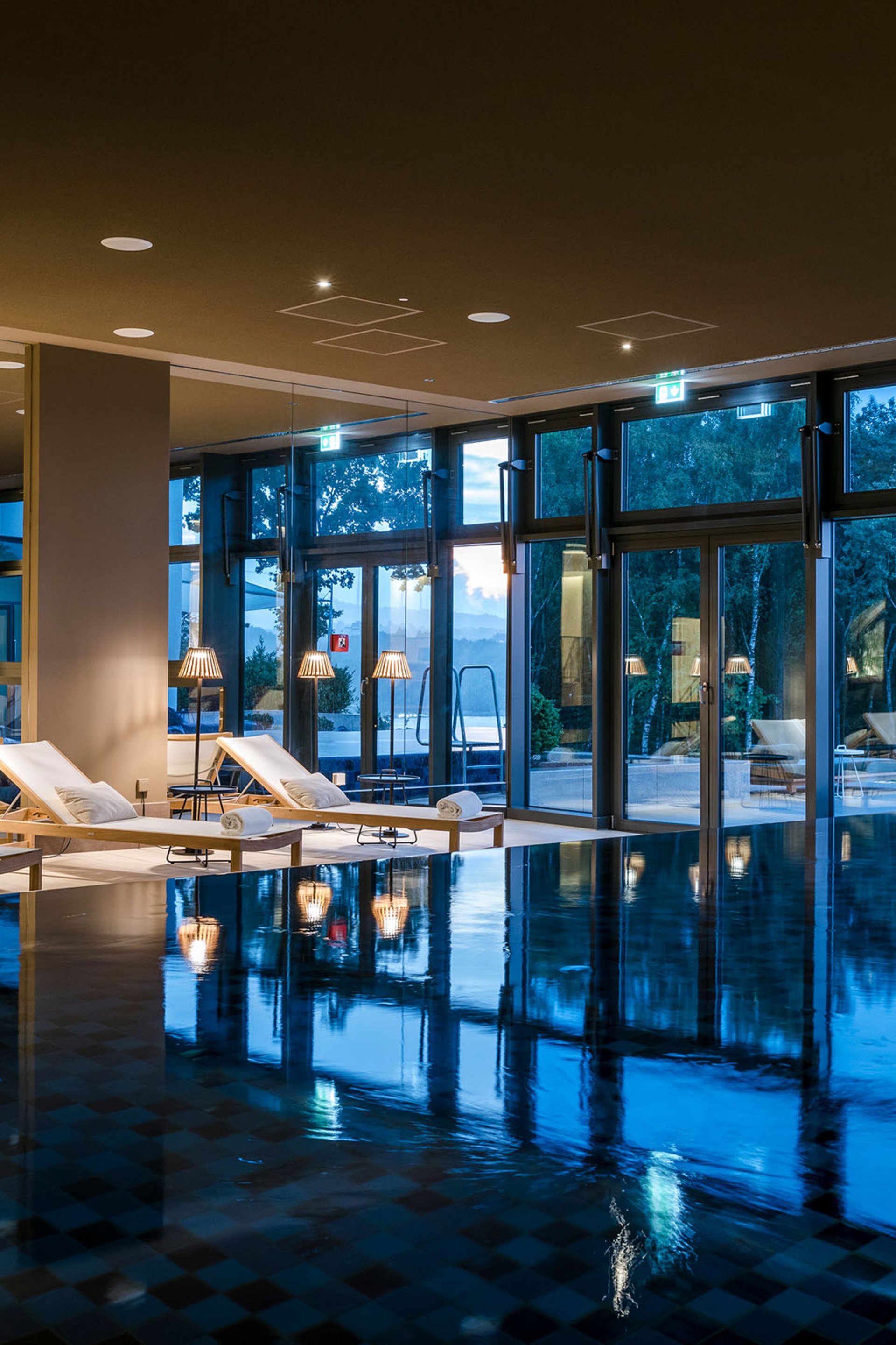Seezeitlodge: Bildergalerie Innenpool mit Liegestühlen und großen Fenstern bei Abenddämmerung