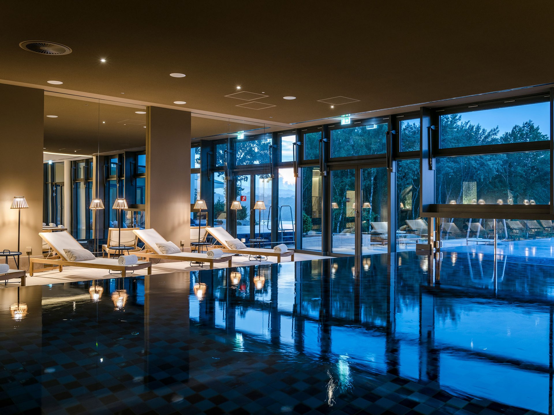 Seezeitlodge: Bildergalerie Innenpool mit Liegestühlen und großen Fenstern bei Abenddämmerung