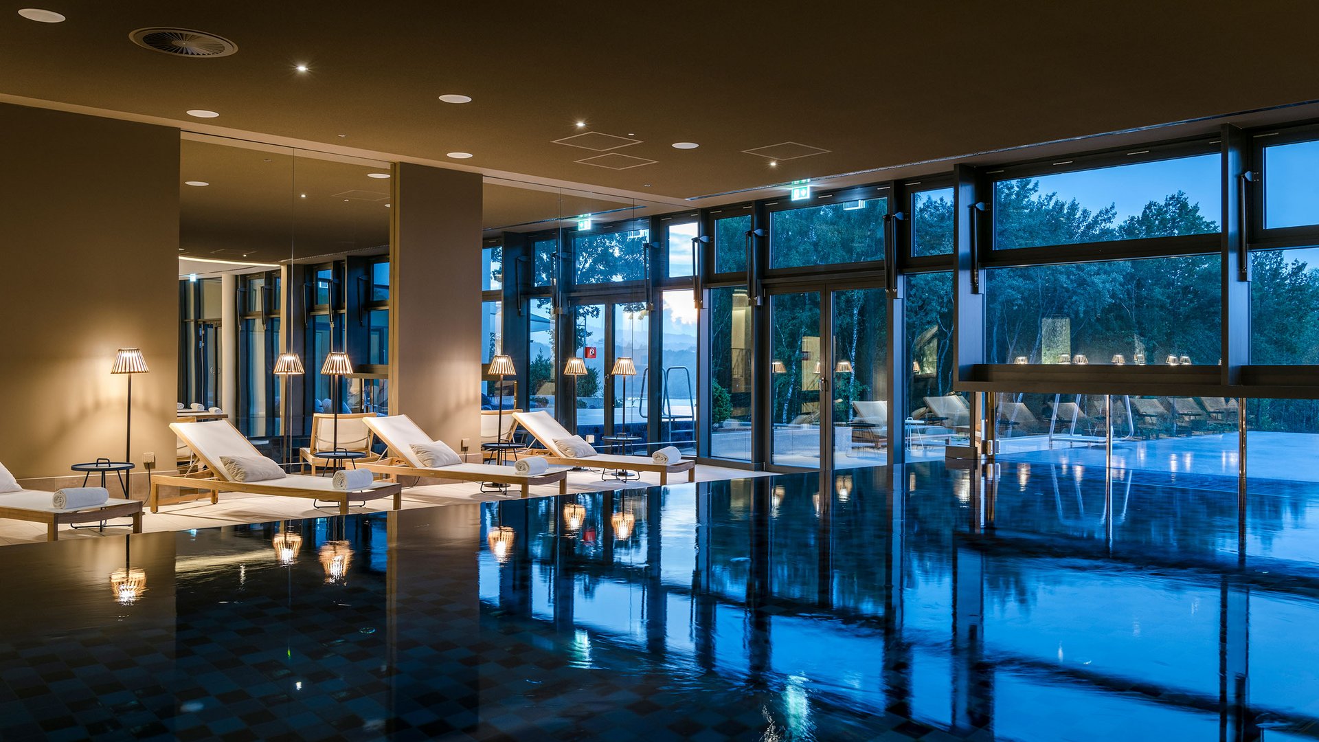Seezeitlodge : Galerie photos Piscine intérieure avec chaises longues et grandes fenêtres au crépuscule