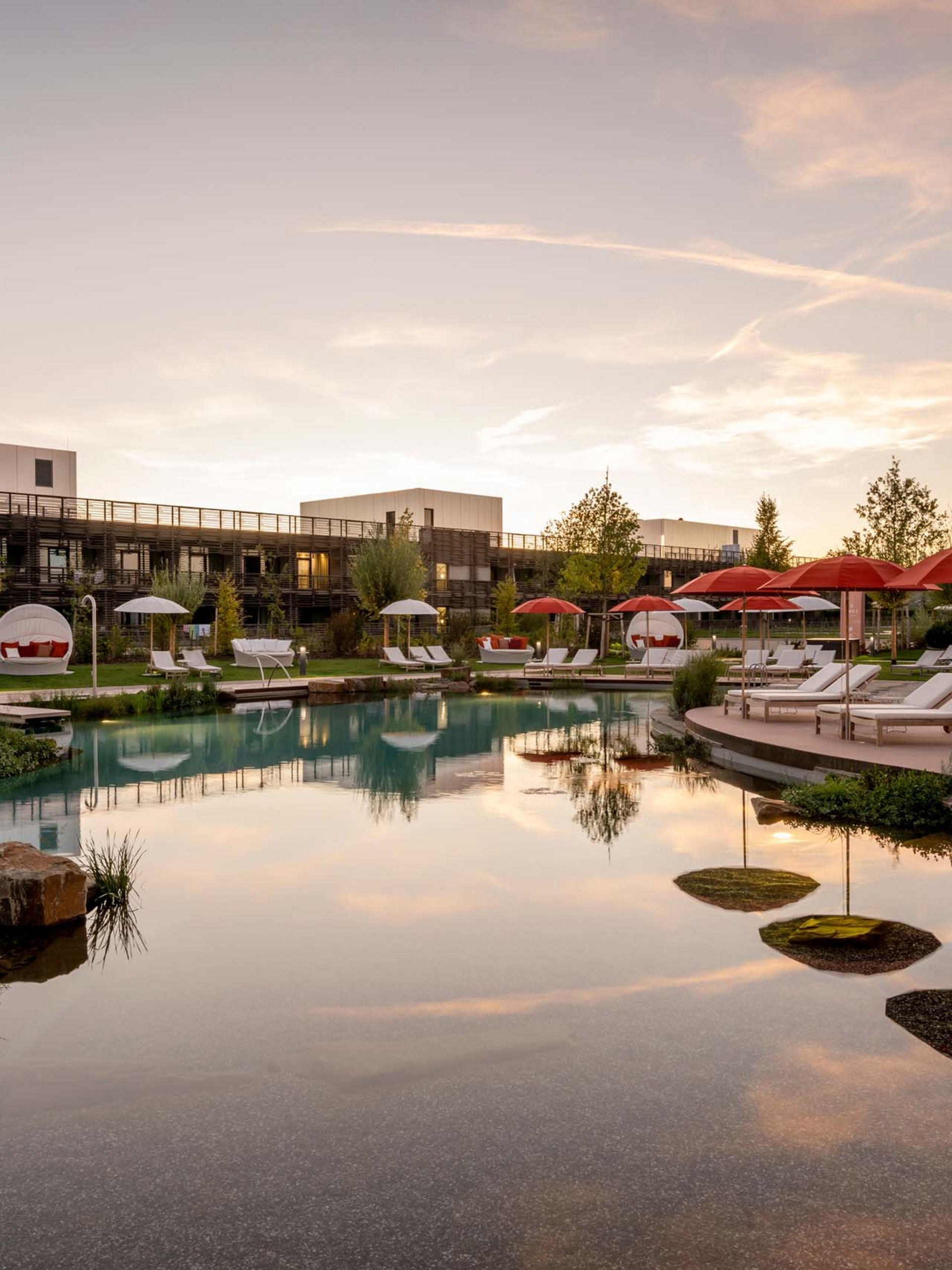 Seezeitlodge : Galerie photos Piscine d'hôtel avec chaises longues et parasols rouges au coucher du soleil
