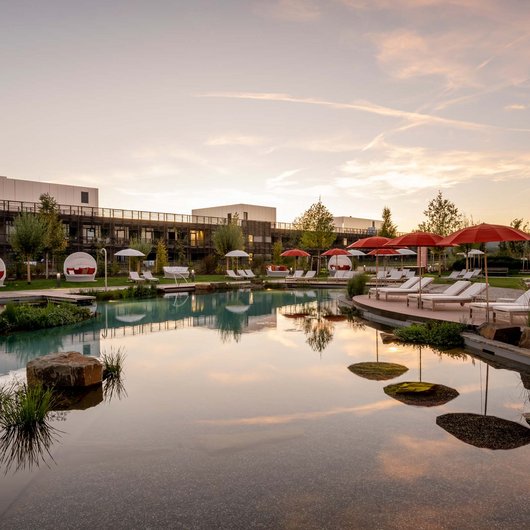 Le Seezeitlodge : votre hôtel au lac de Bostal Piscine d'hôtel avec chaises longues et parasols rouges au coucher du soleil
