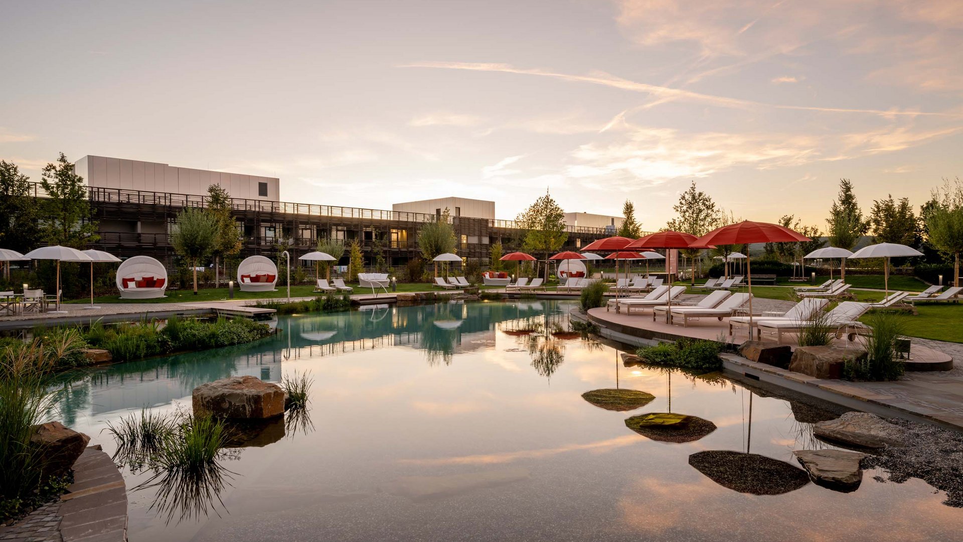 Seezeitlodge : Day Spa au bord du lac de Bostal Piscine d'hôtel avec chaises longues et parasols rouges au coucher du soleil