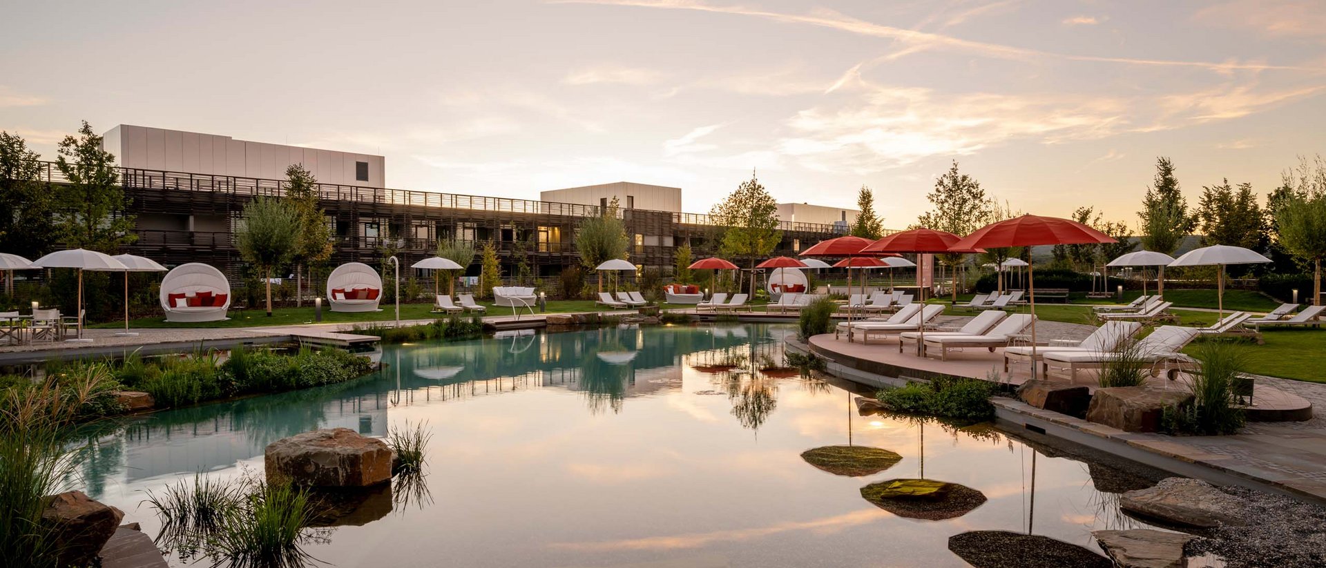 Seezeitlodge : Galerie photos Piscine d'hôtel avec chaises longues et parasols rouges au coucher du soleil