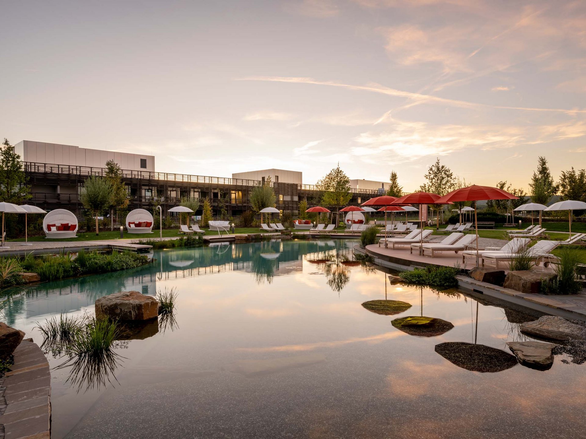 Seezeitlodge: Bildergalerie Hotelpool mit Liegen und roten Sonnenschirmen bei Sonnenuntergang
