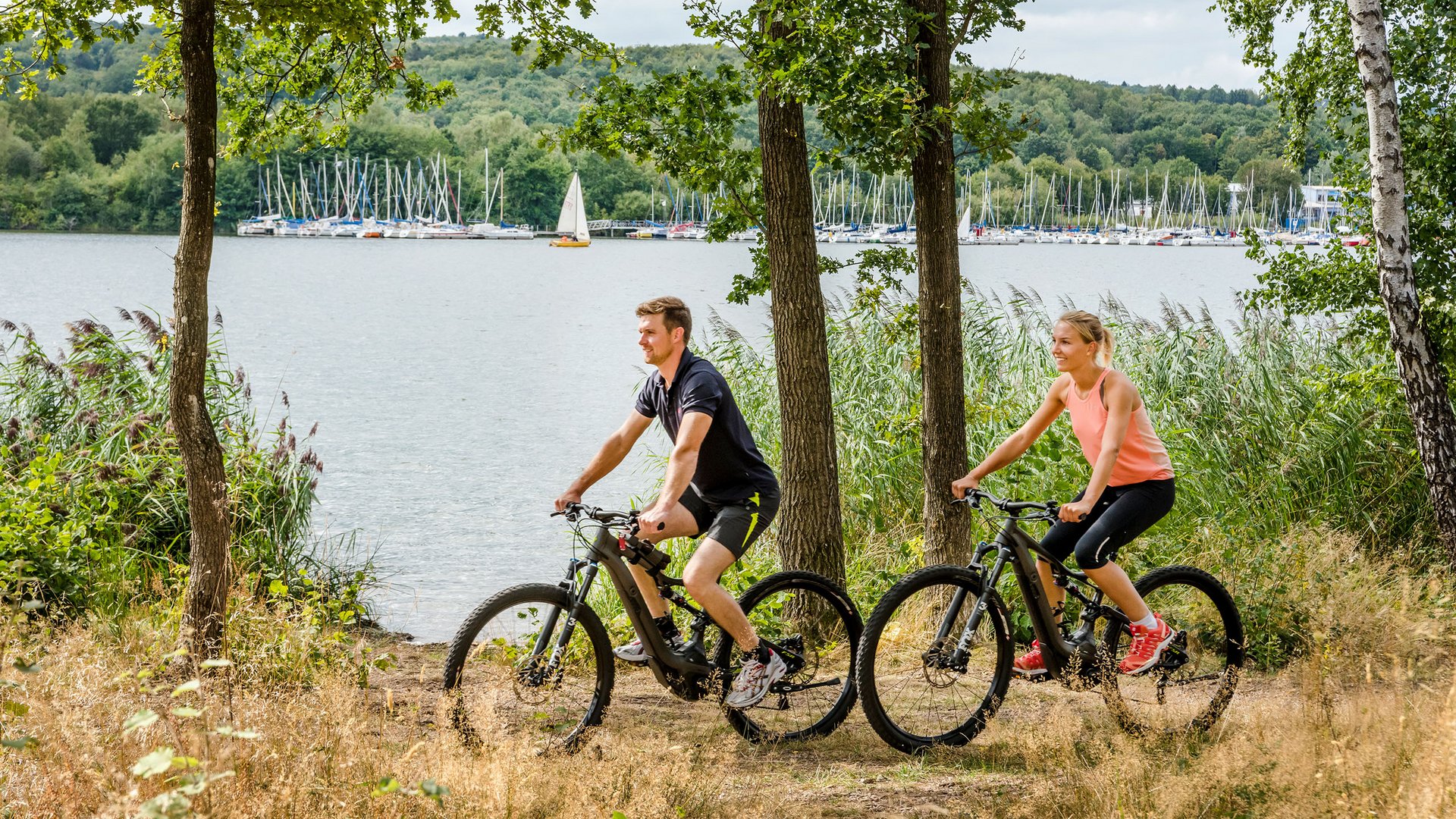 Seezeitlodge : Galerie photos Couple fait du VTT au bord d'un lac avec voiliers en arrière-plan