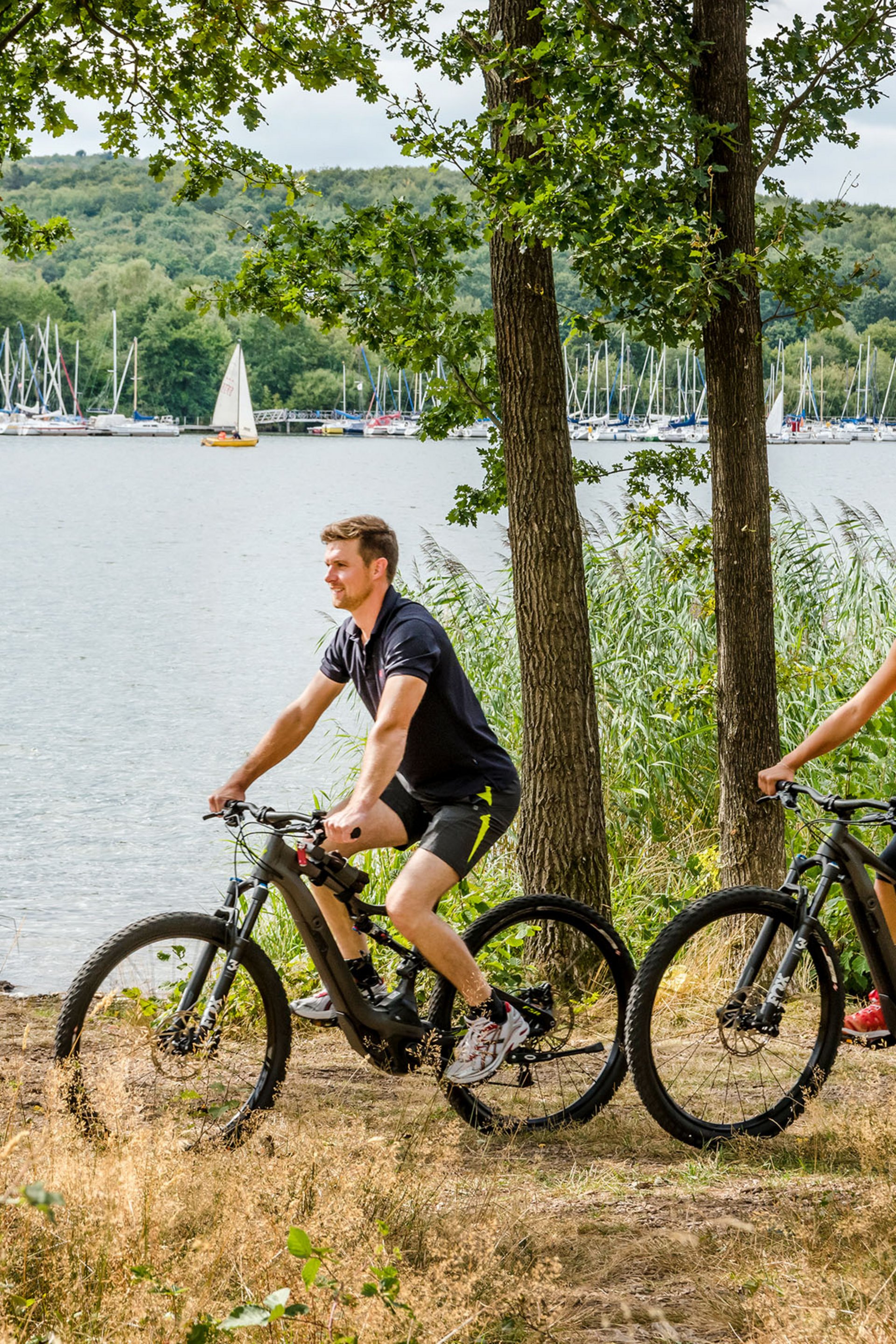 Seezeitlodge : Galerie photos Couple fait du VTT au bord d'un lac avec voiliers en arrière-plan