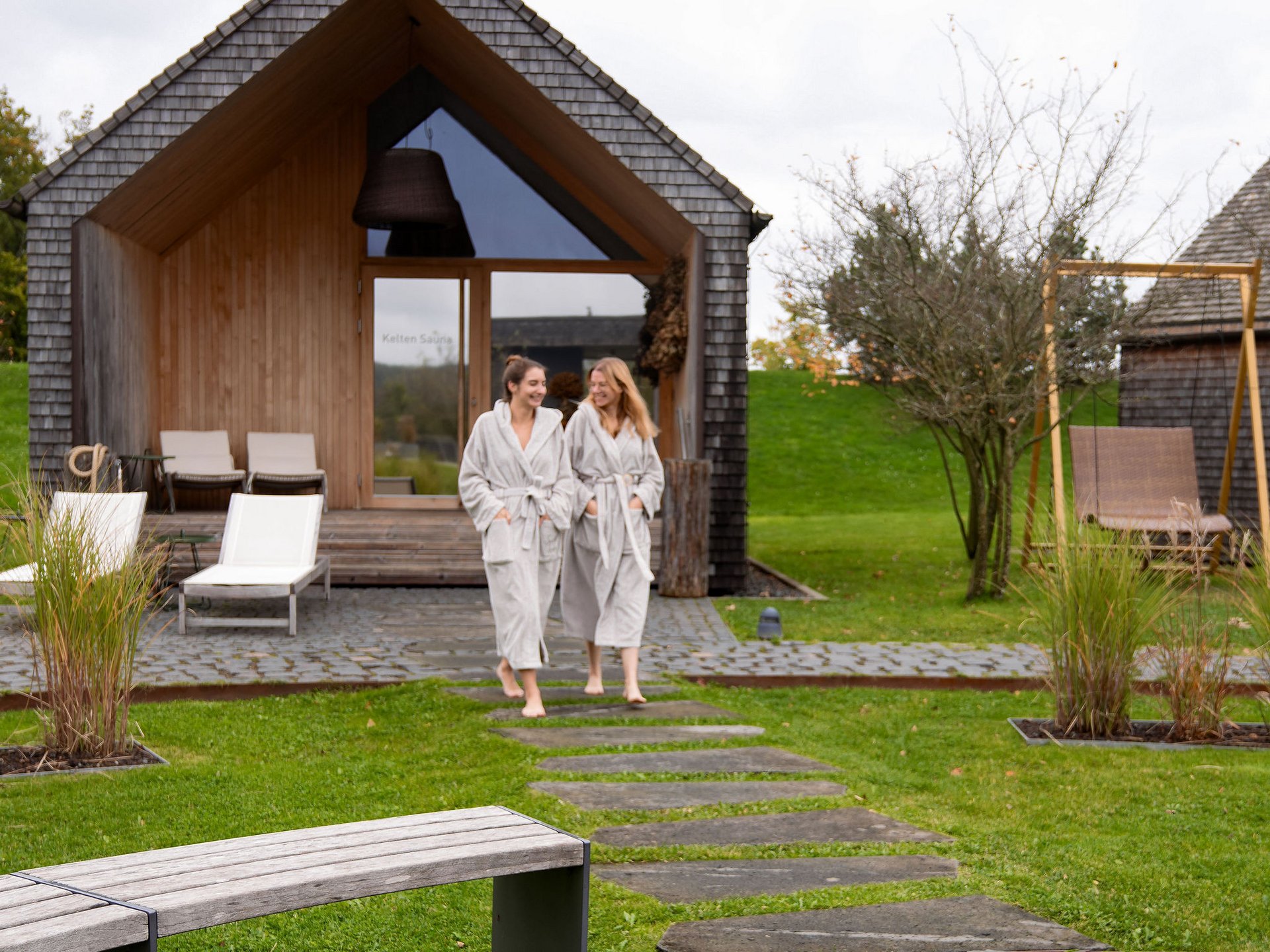 Seezeitlodge : Galerie photos Deux femmes en peignoirs devant un sauna moderne dans un cadre verdoyant