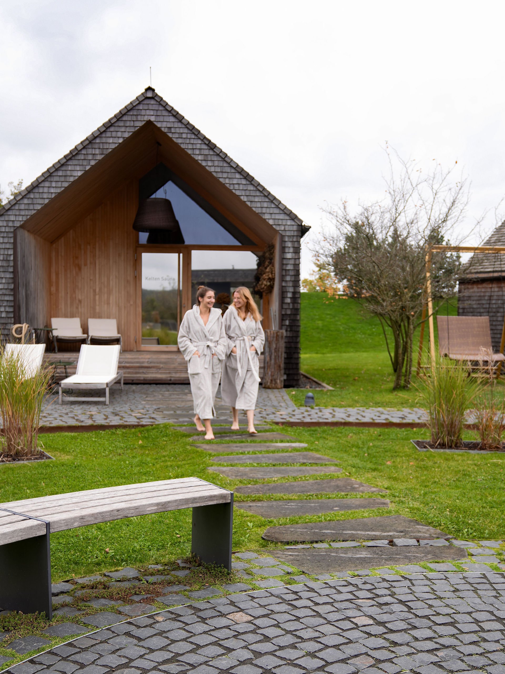 Seezeitlodge : Galerie photos Deux femmes en peignoirs devant un sauna moderne dans un cadre verdoyant
