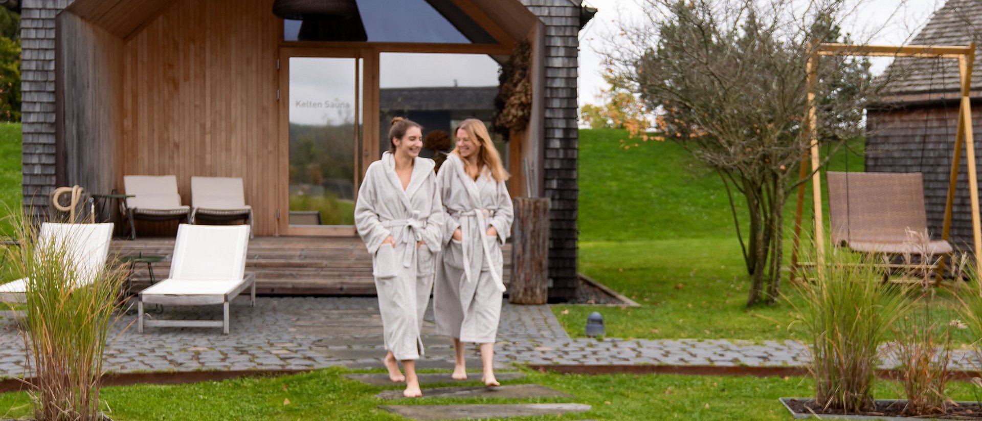 Seezeitlodge: Bildergalerie Zwei Frauen in Bademänteln vor einer modernen Sauna im Grünen