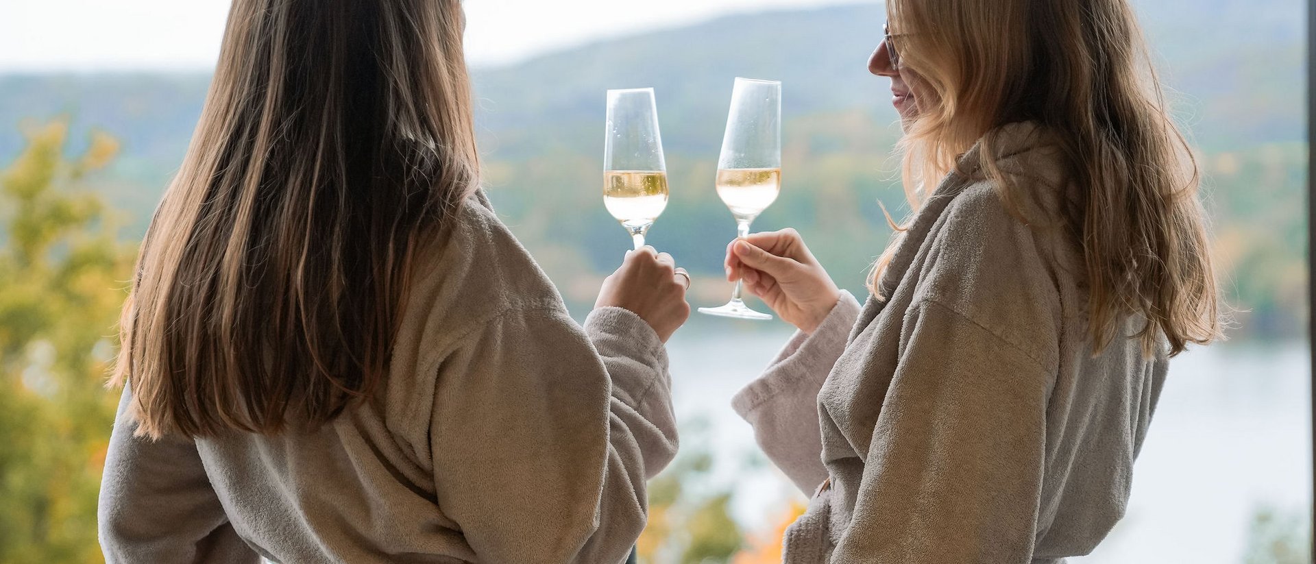 Seezeitlodge: Bildergalerie Zwei Frauen in Bademänteln stoßen mit Weingläsern auf einer Terrasse an