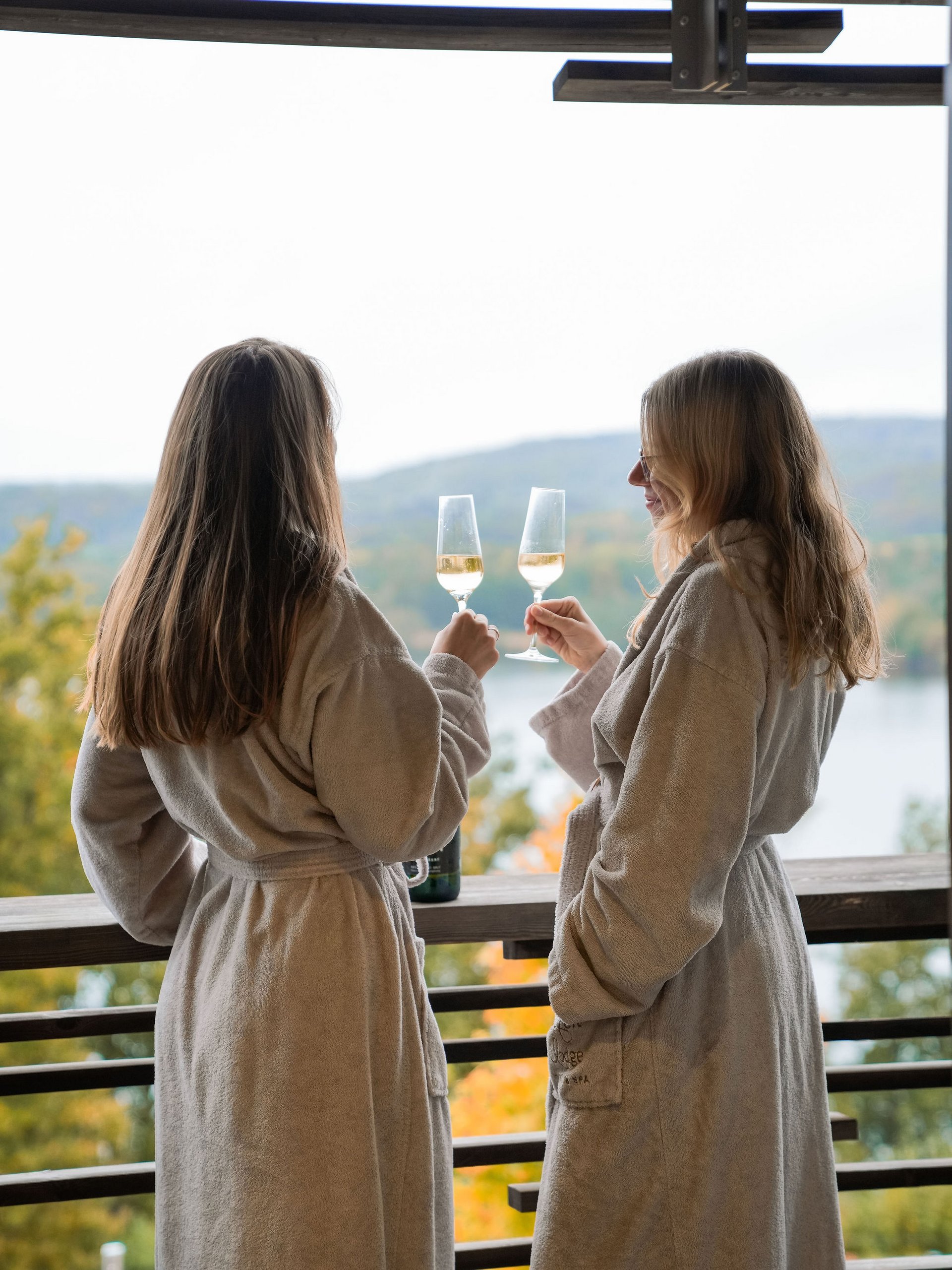 Seezeitlodge: Bildergalerie Zwei Frauen in Bademänteln stoßen mit Weingläsern auf einer Terrasse an