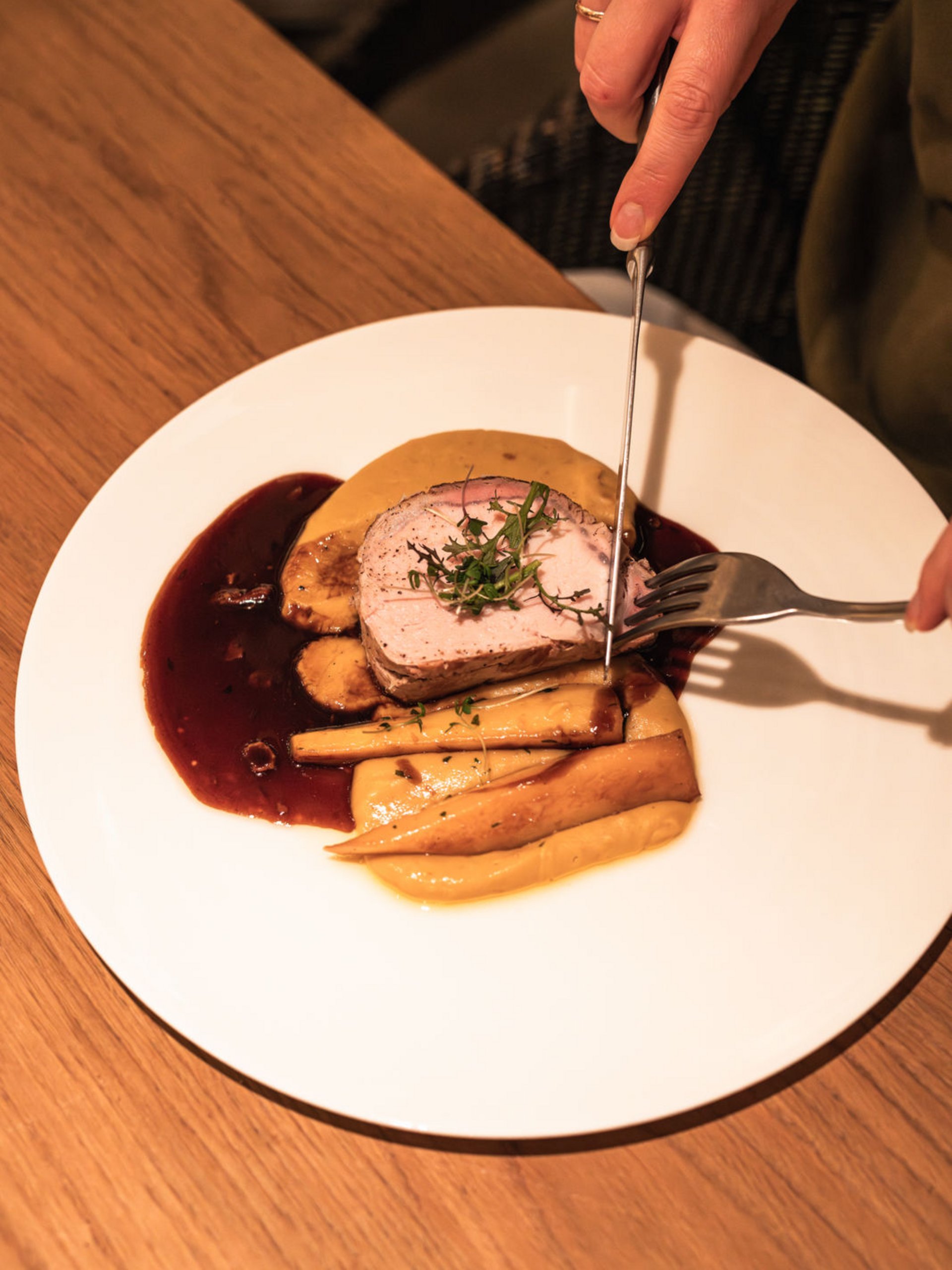 Seezeitlodge : Galerie photos Person coupe de la viande rôtie avec garniture et sauce dans une assiette blanche