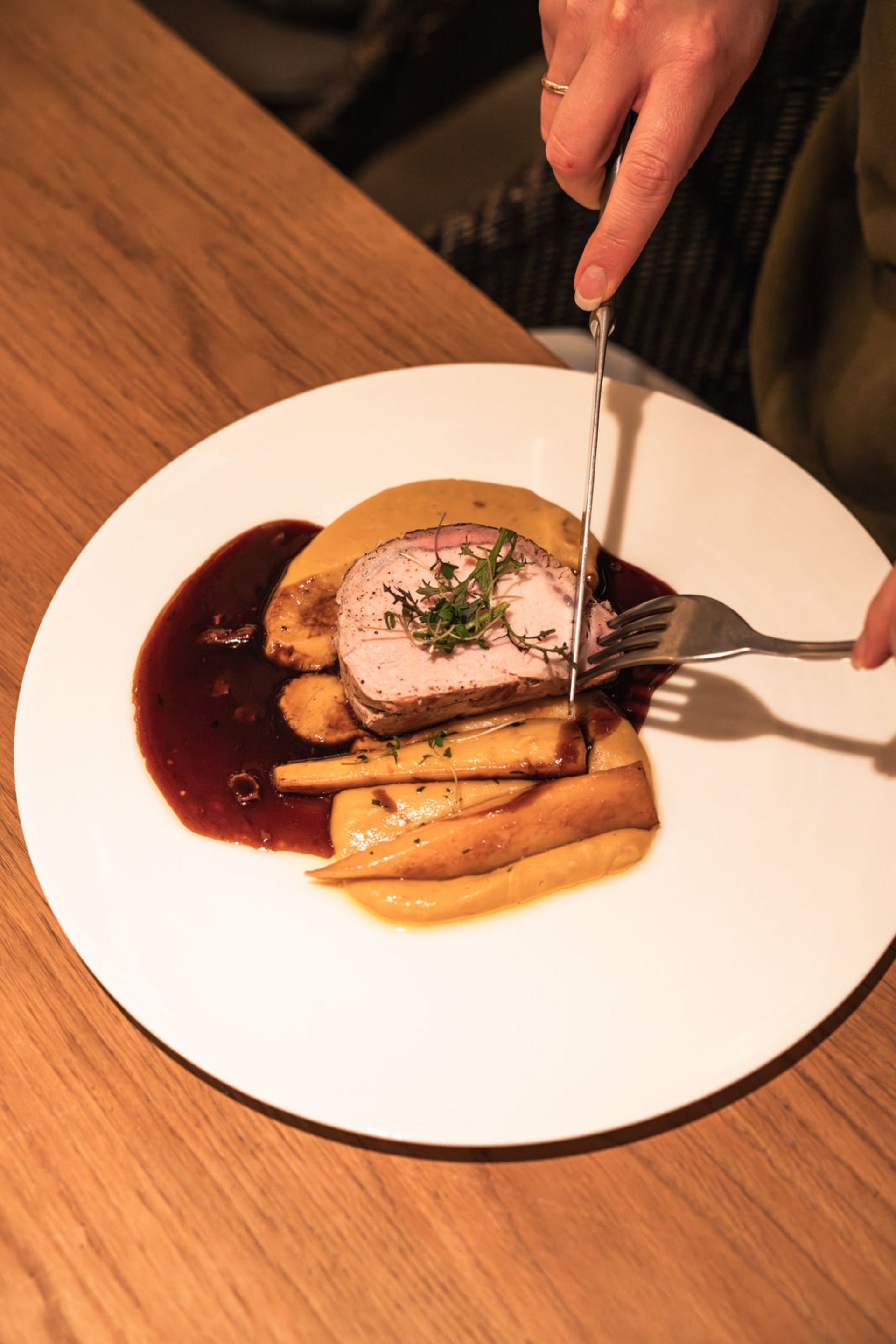 Seezeitlodge : Galerie photos Person coupe de la viande rôtie avec garniture et sauce dans une assiette blanche
