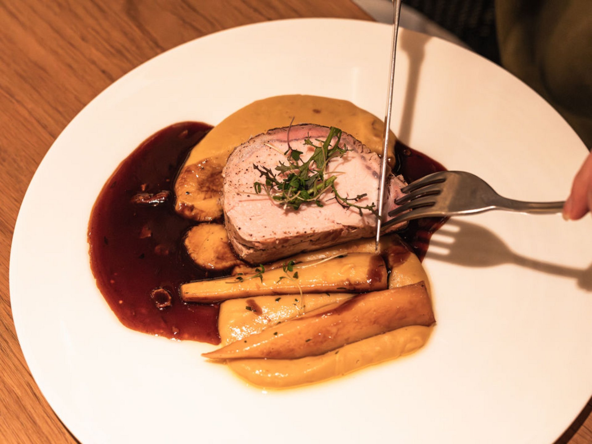 Le Seezeitlodge : votre hôtel au lac de Bostal Person coupe de la viande rôtie avec garniture et sauce dans une assiette blanche