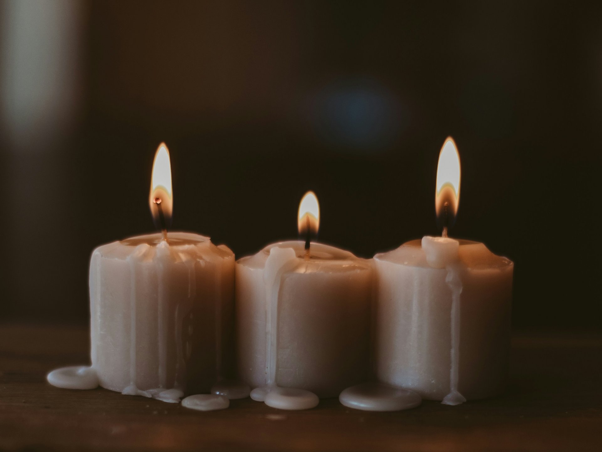 Yule - Keltische Feiertage im Porträt | Seezeitlodge Hotel & Spa Bostalsee Drei brennende weiße Kerzen mit schmelzendem Wachs auf dunklem Hintergrund