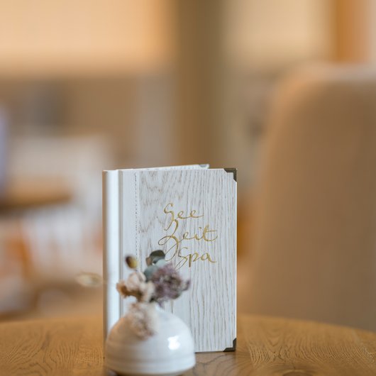 Seezeitlodge: Bar & Bistros Weißes Spa-Menü und kleine Vase mit Trockenblumen auf Holztisch