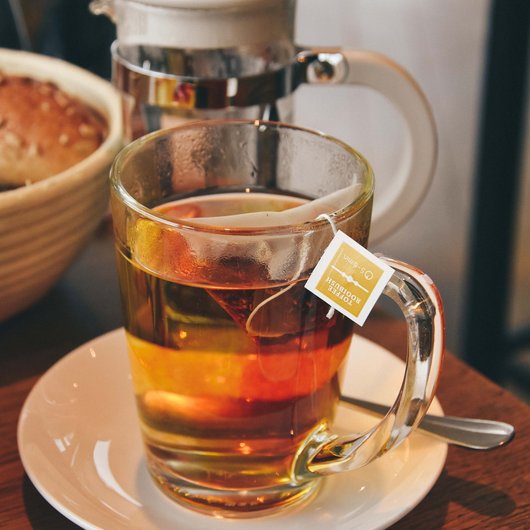 Echter Genuss am Bostalsee Tasse mit heißem Tee und Teebeutel auf einem weißen Unterteller mit Löffel