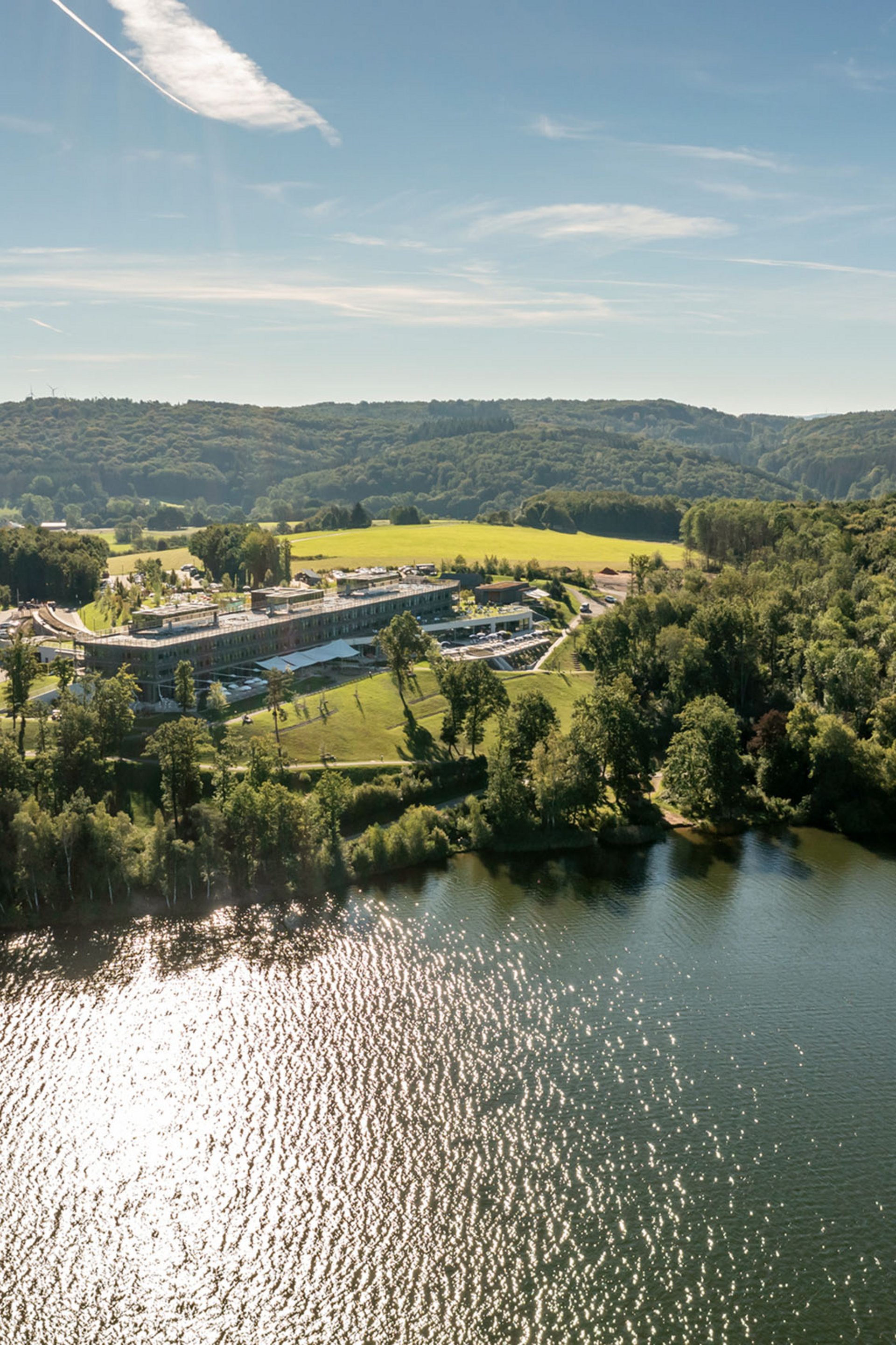 Seezeitlodge : Galerie photos Vue aérienne d'un lac avec des rives boisées et un grand bâtiment sous le soleil