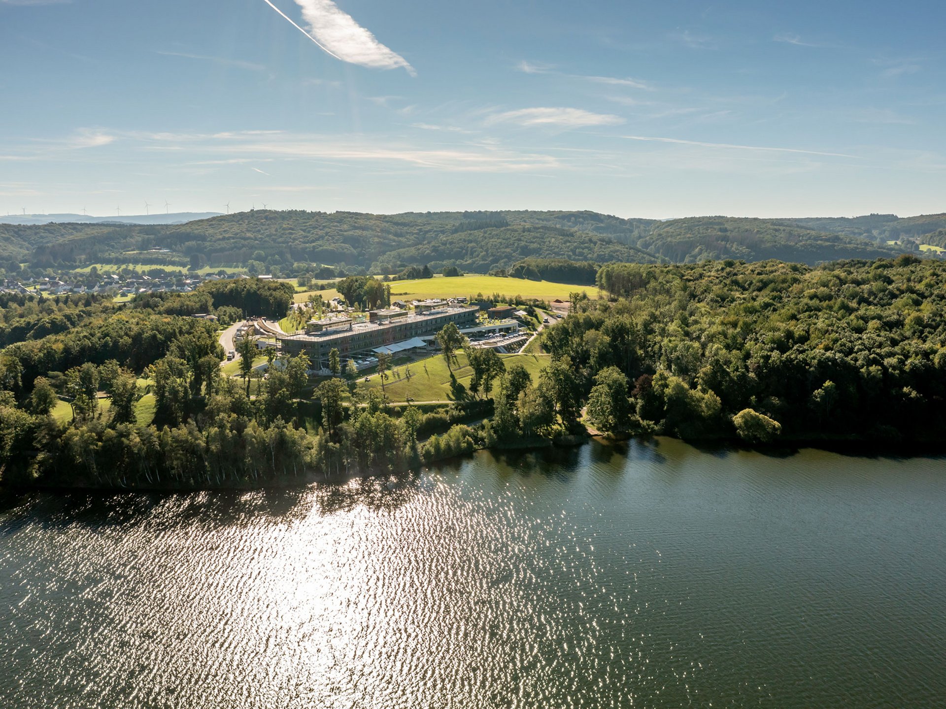 Urlaub am Bostalsee: die Highlights der Region Luftaufnahme eines Sees mit bewaldeten Ufern und einem großen Gebäude bei Sonnenschein