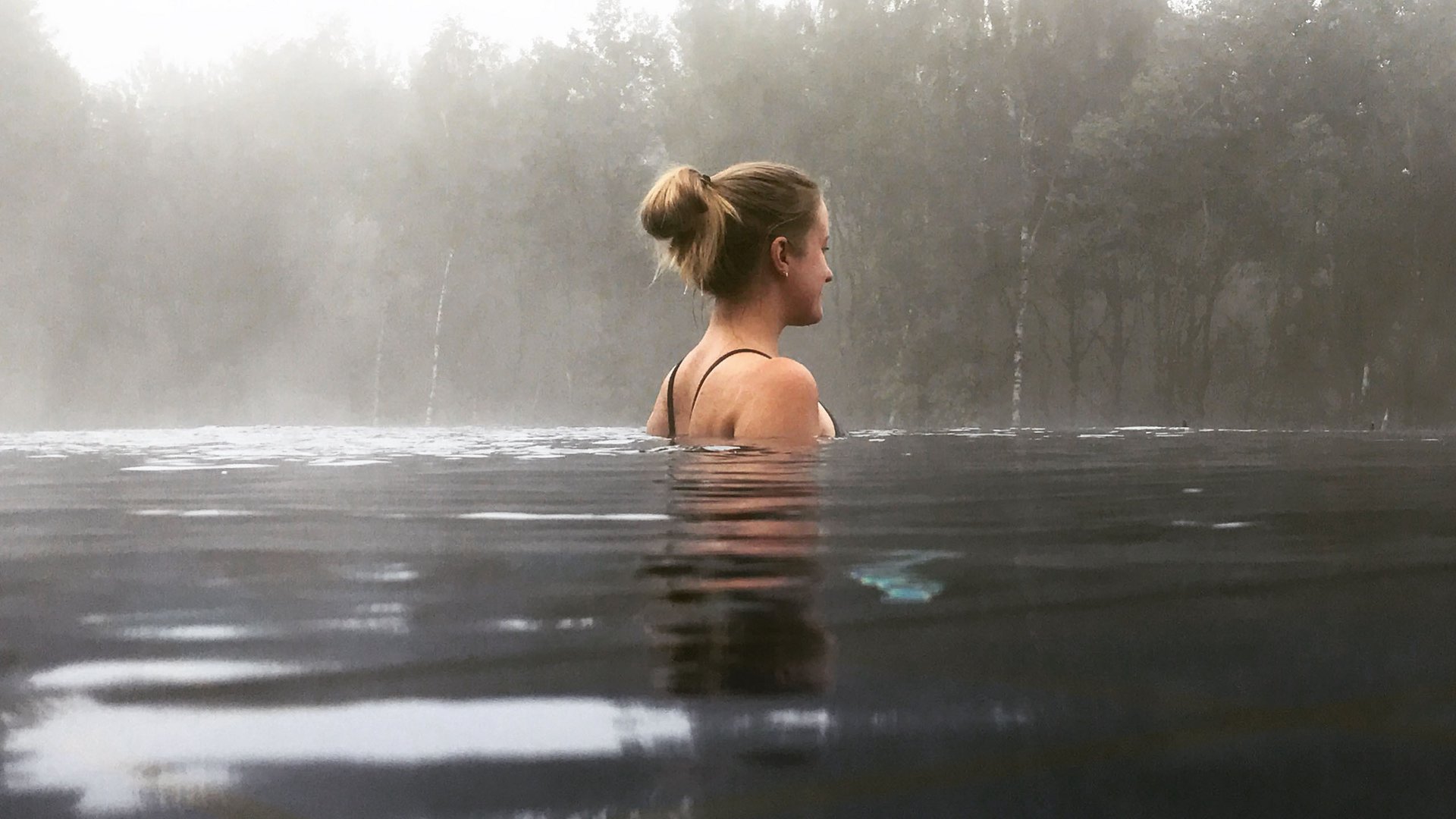 Seezeitlodge : Galerie photos Femme se détendant dans l'eau avec brouillard et arbres en arrière-plan