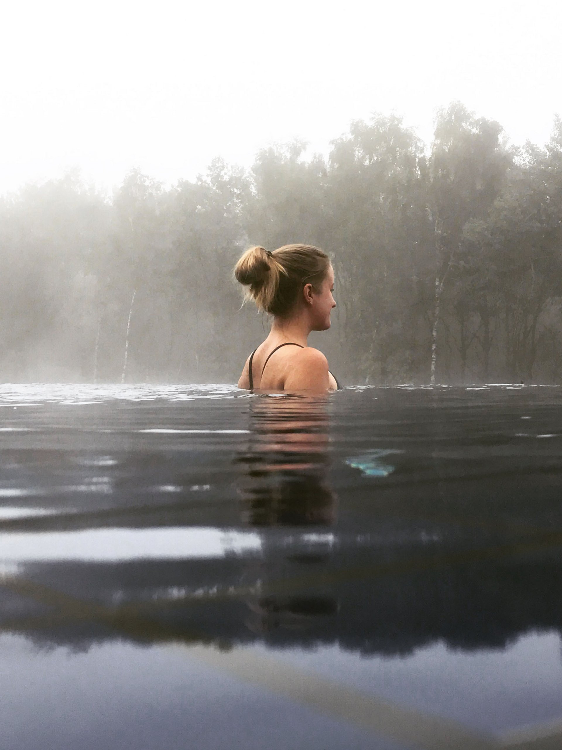 Seezeitlodge : Galerie photos Femme se détendant dans l'eau avec brouillard et arbres en arrière-plan