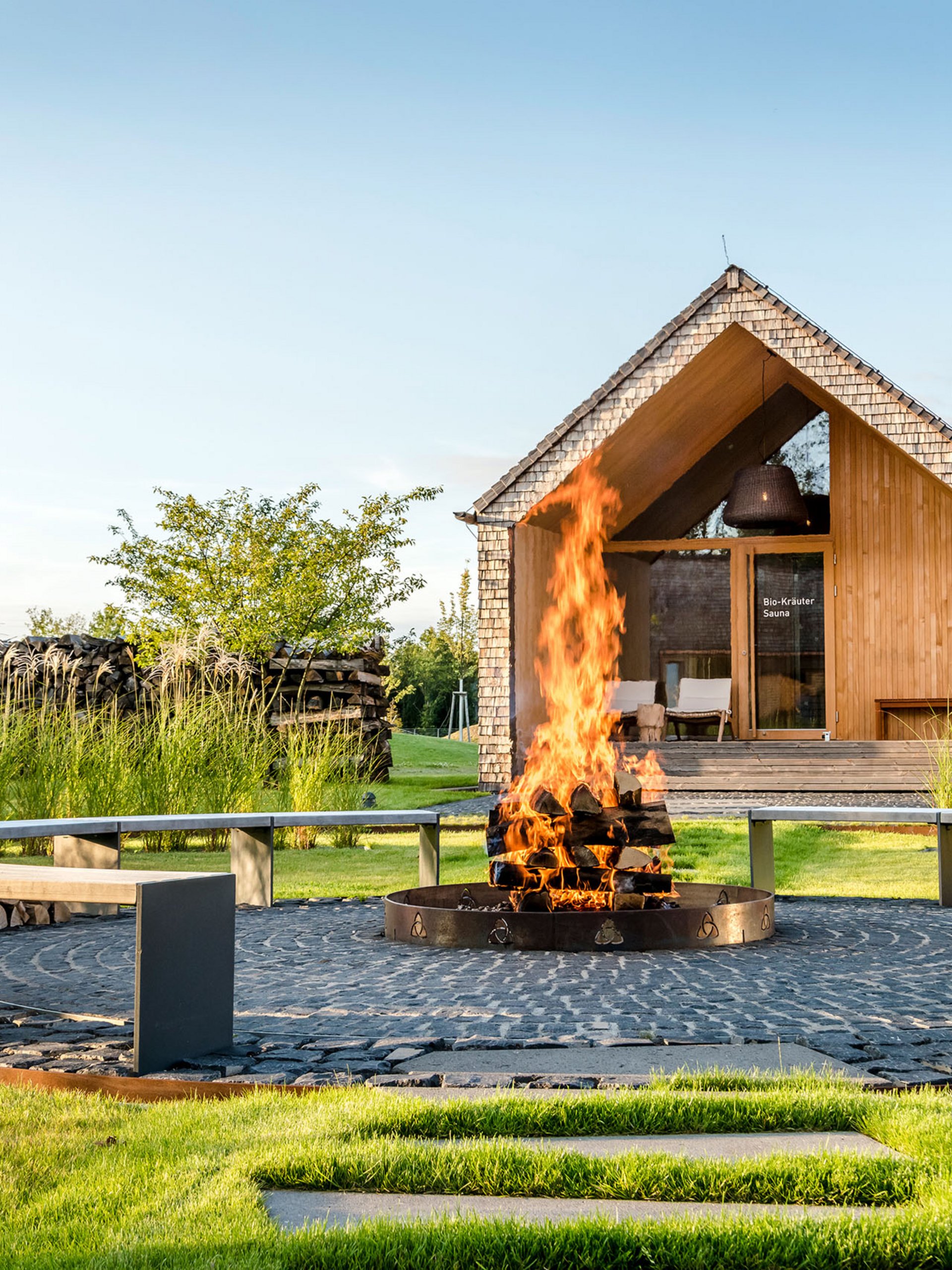 Seezeitlodge : Galerie photos Foyer avec bois en feu et banc circulaire devant un sauna en bois