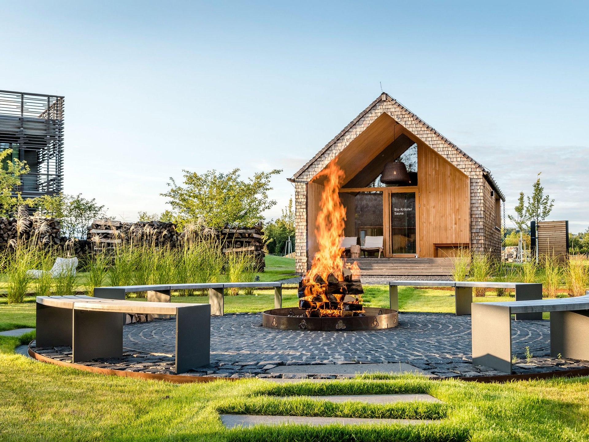Seezeitlodge : Galerie photos Foyer avec bois en feu et banc circulaire devant un sauna en bois