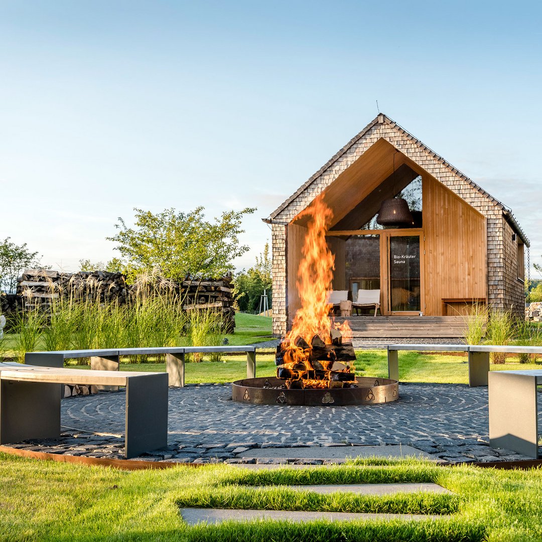 Seezeitlodge : protection des données Foyer avec bois en feu et banc circulaire devant un sauna en bois
