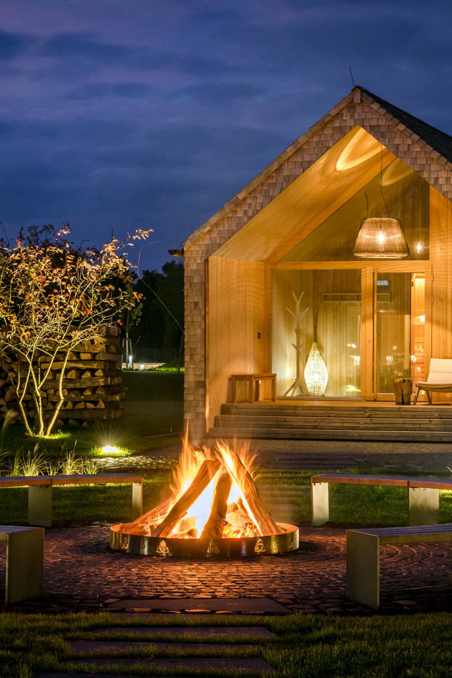 Seezeitlodge: Bildergalerie Holzhaus bei Nacht mit Lagerfeuer und Sitzbänken im Garten