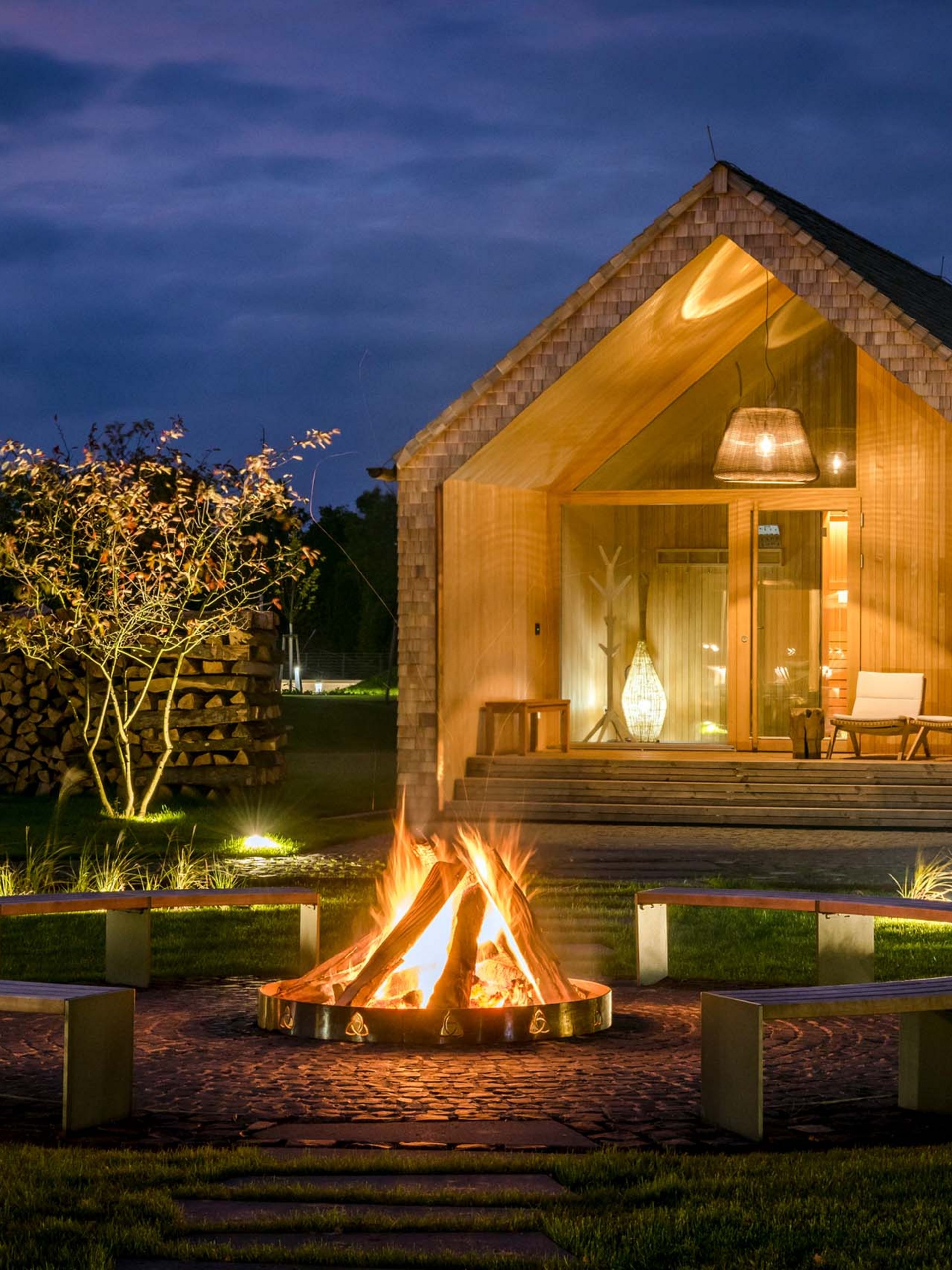 Seezeitlodge : Galerie photos Maison en bois de nuit avec feu de camp et bancs dans le jardin