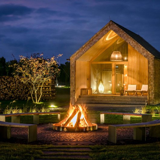 Seezeitlodge: Ihr Spa-Hotel am Bostalsee Holzhaus bei Nacht mit Lagerfeuer und Sitzbänken im Garten