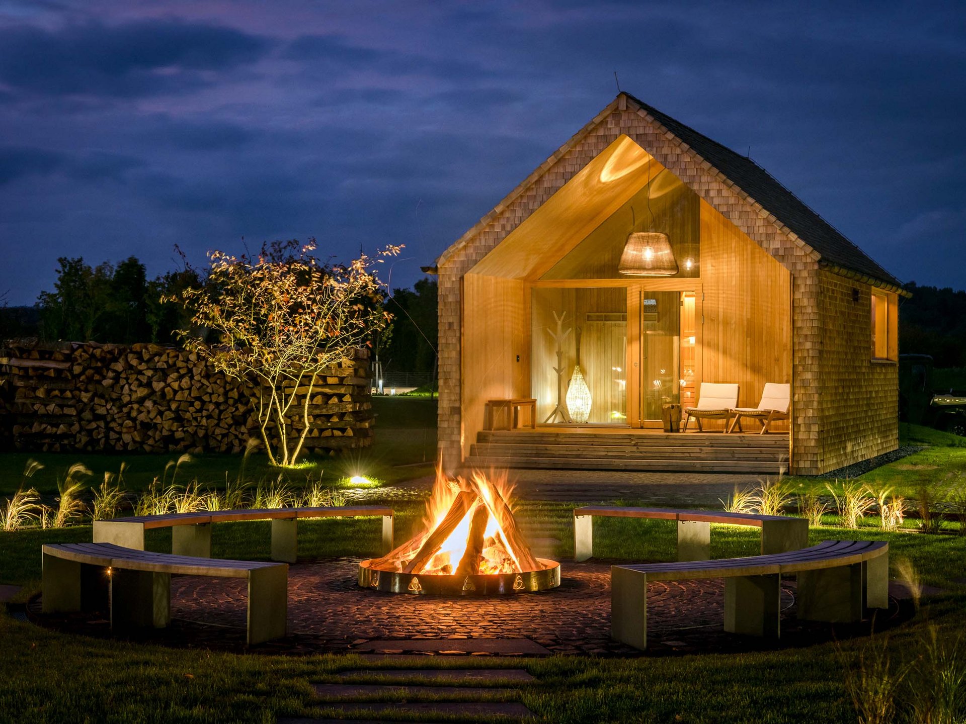 Seezeitlodge: Bildergalerie Holzhaus bei Nacht mit Lagerfeuer und Sitzbänken im Garten